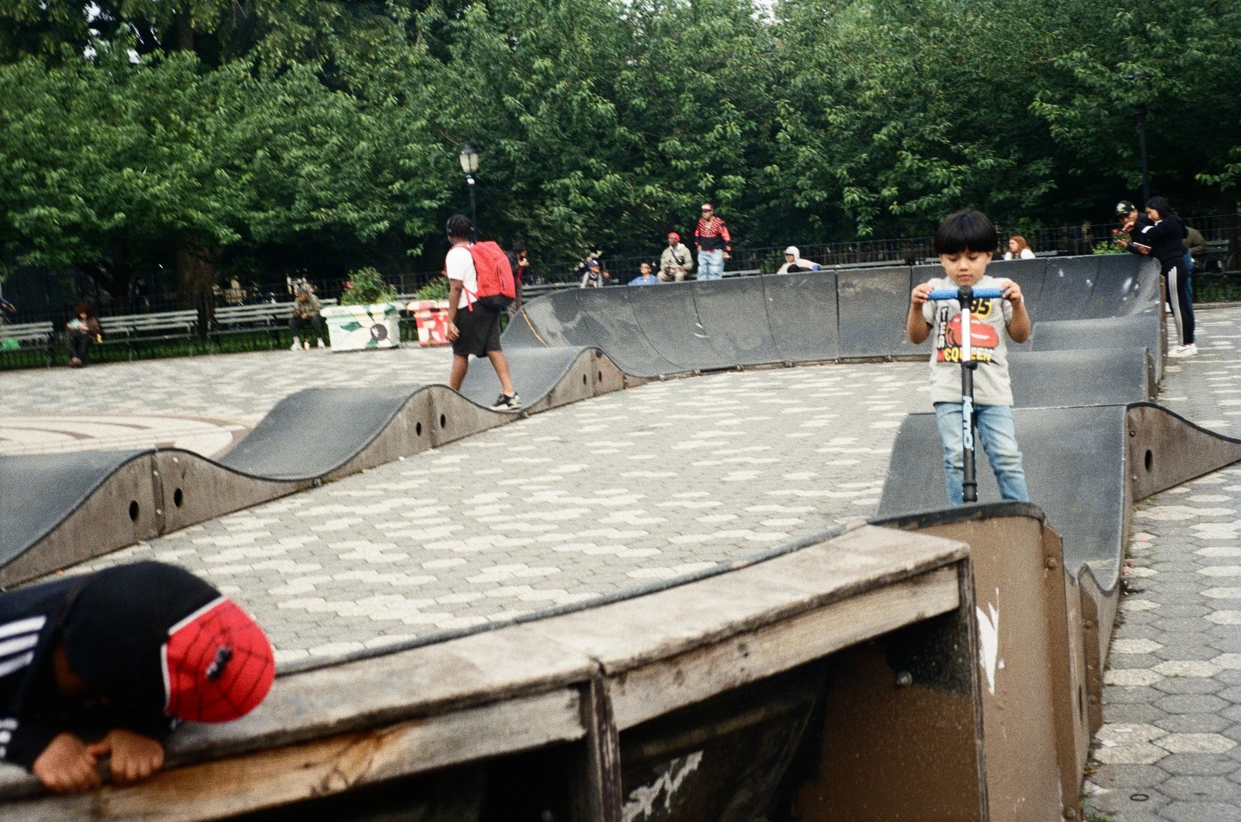 Children playing on skate park ramps in a park with trees.