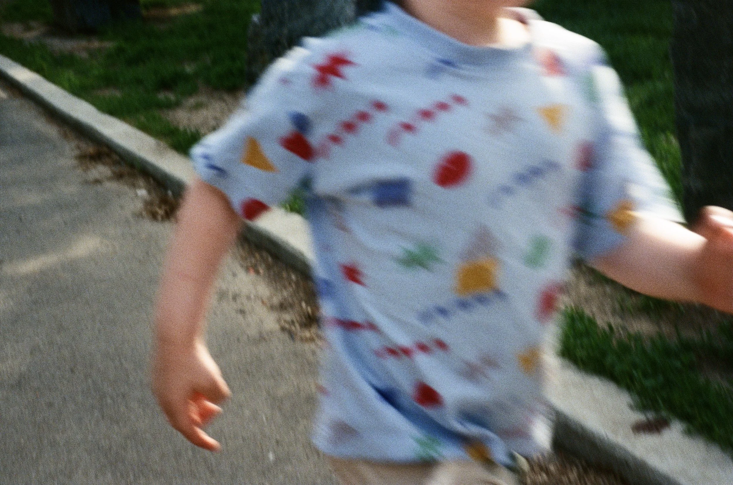 A child running outdoors wearing a white shirt with colorful shapes and patterns.