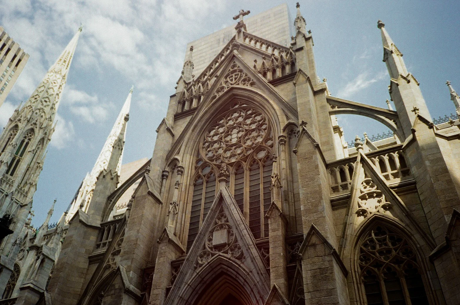 Looking up at the exterior of a Gothic cathedral with detailed stonework, pointed arches, and tall spires against a partly cloudy sky.