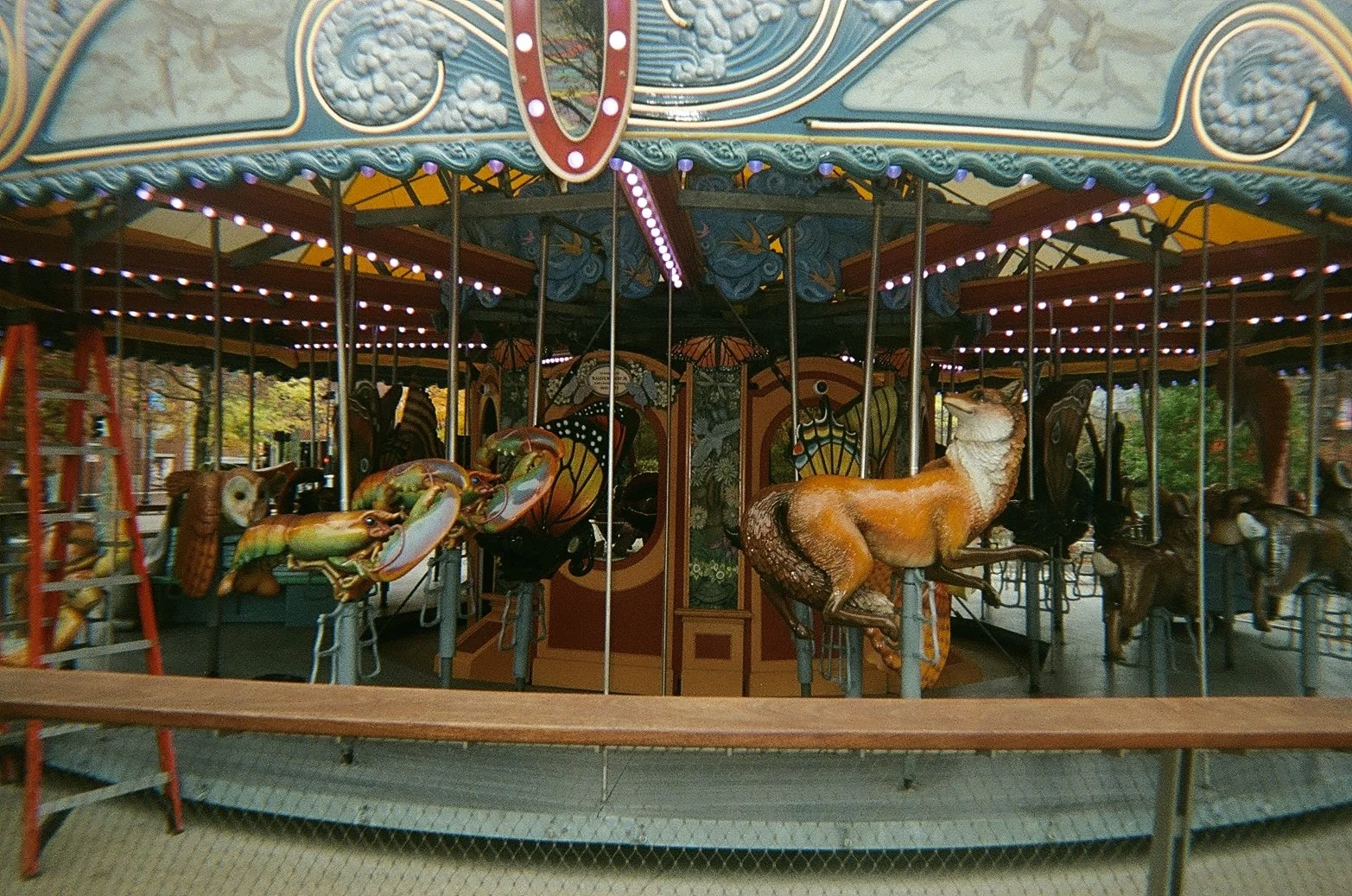 Colorful vintage carousel with painted animals, including a horse, set outdoors surrounded by trees.