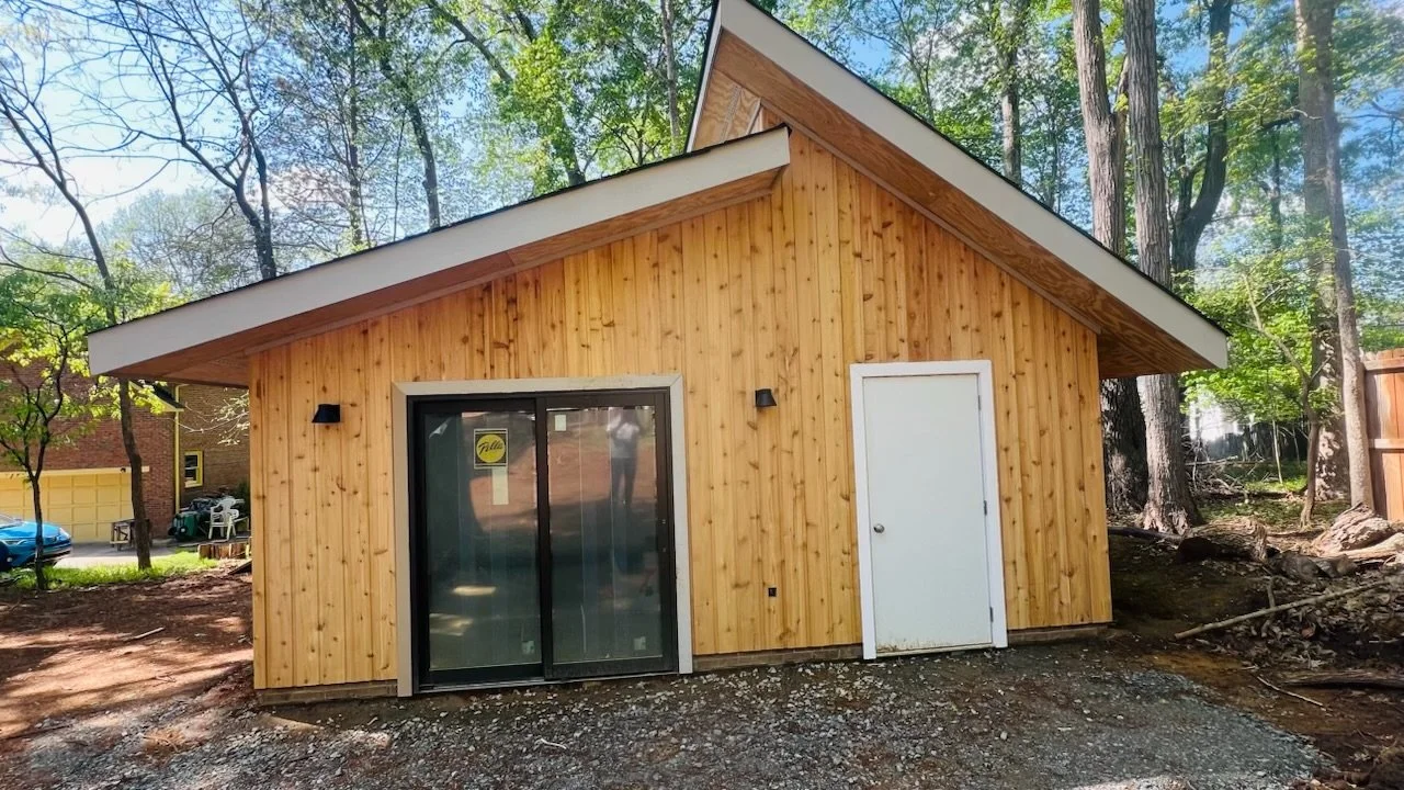 Small wooden siding home with sliding glass patio doors and a white side door, situated in a yard with trees.