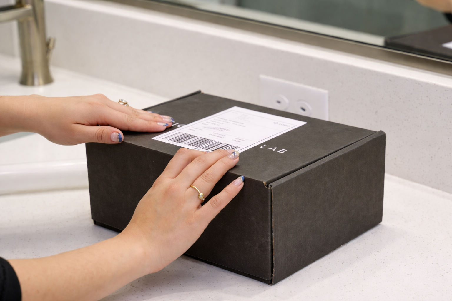 Hands handling a black box with a shipping label on a beige countertop.
