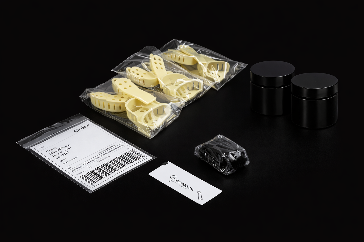 Dental impression materials, including yellow plastic tray inserts in clear bags, a black rubber base, and an order form on a black surface.