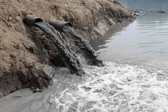 Pipe releasing muddy water into a body of water near the shoreline.
