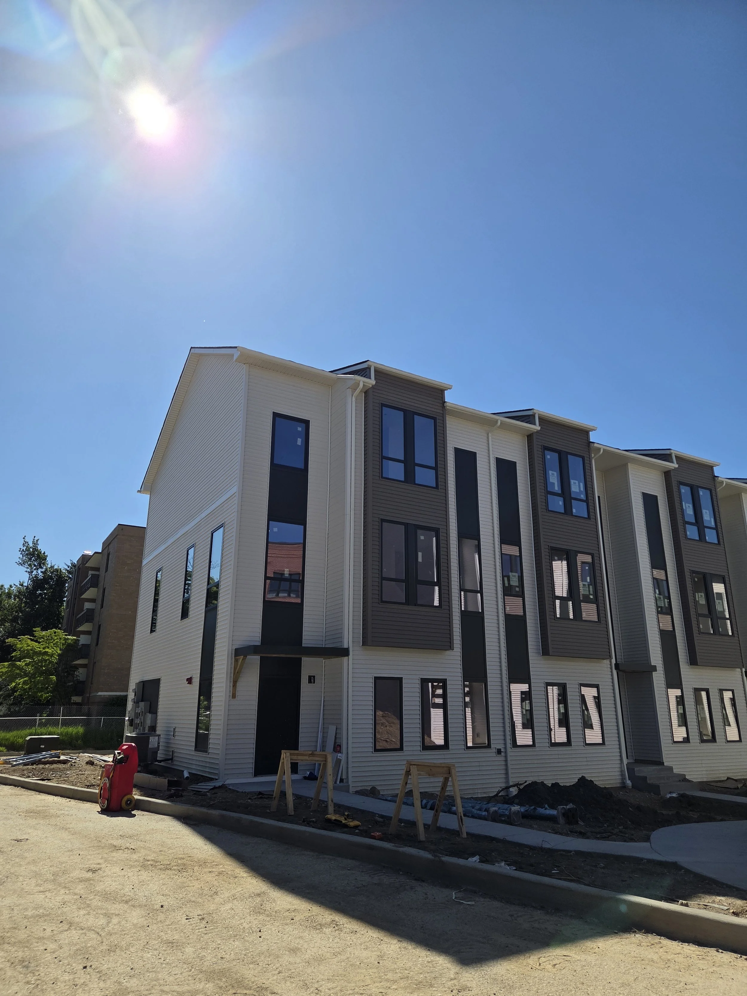Under construction multi-story residential building with white and dark gray siding, large windows, and a clear blue sky with the sun shining.