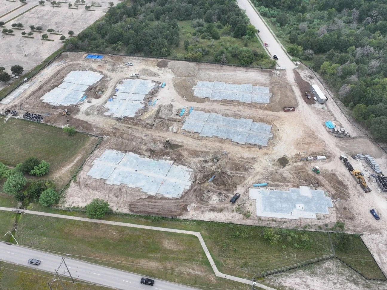 Aerial view of a construction site with multiple building foundations in progress, surrounded by trees and roads.