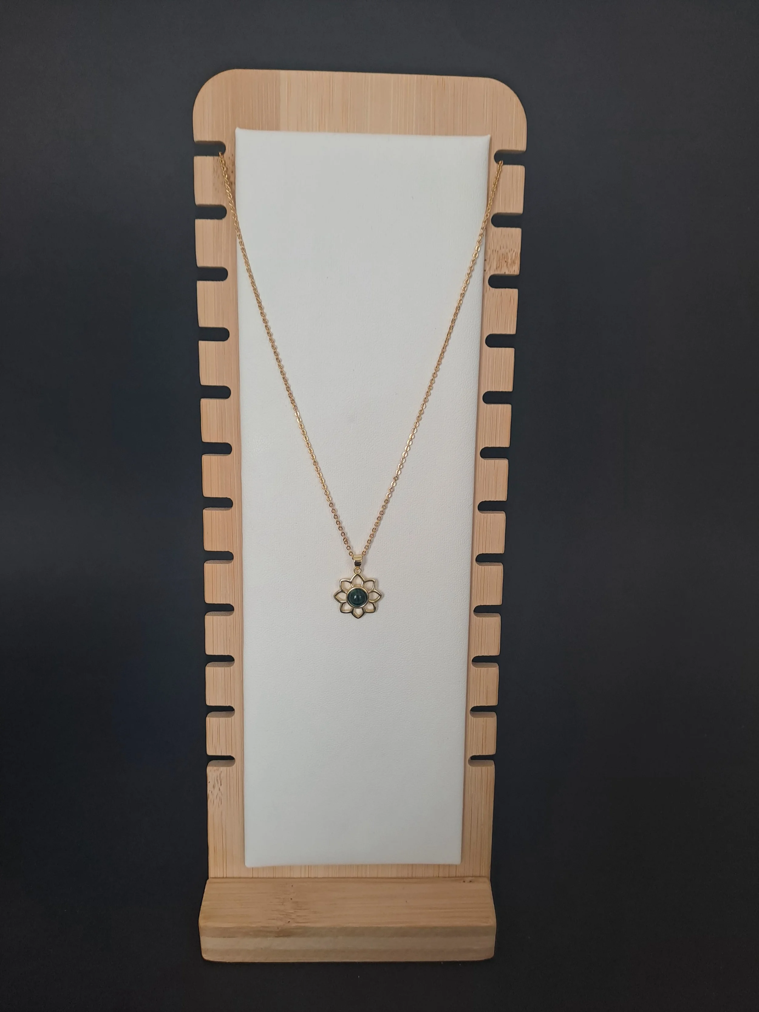 Collier en or avec pendentif en forme de fleur et pierre verte, exposé sur un support en bois avec un fond noir.
