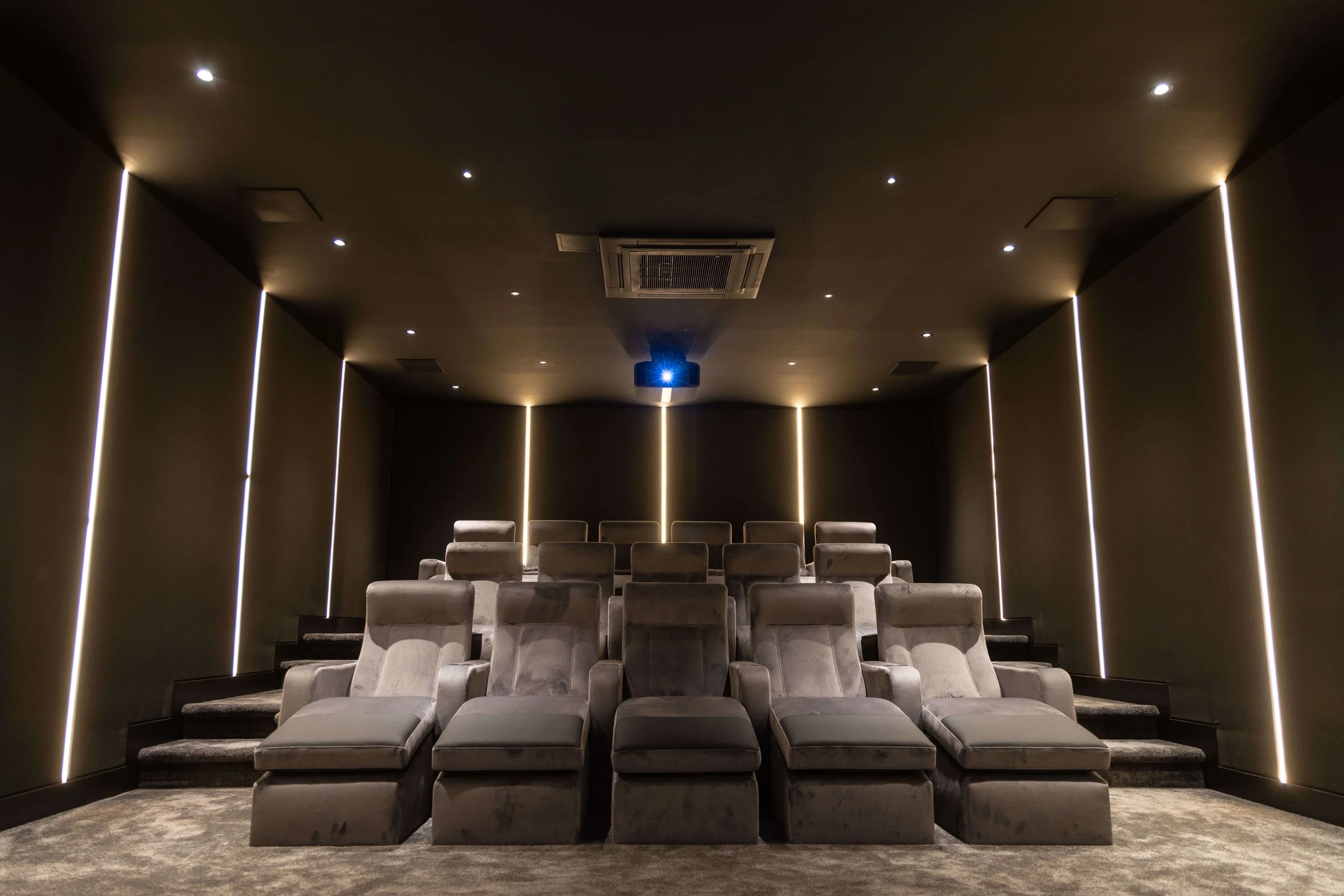 Luxury movie theater with plush reclining chairs, dark walls, and a ceiling-mounted projector.