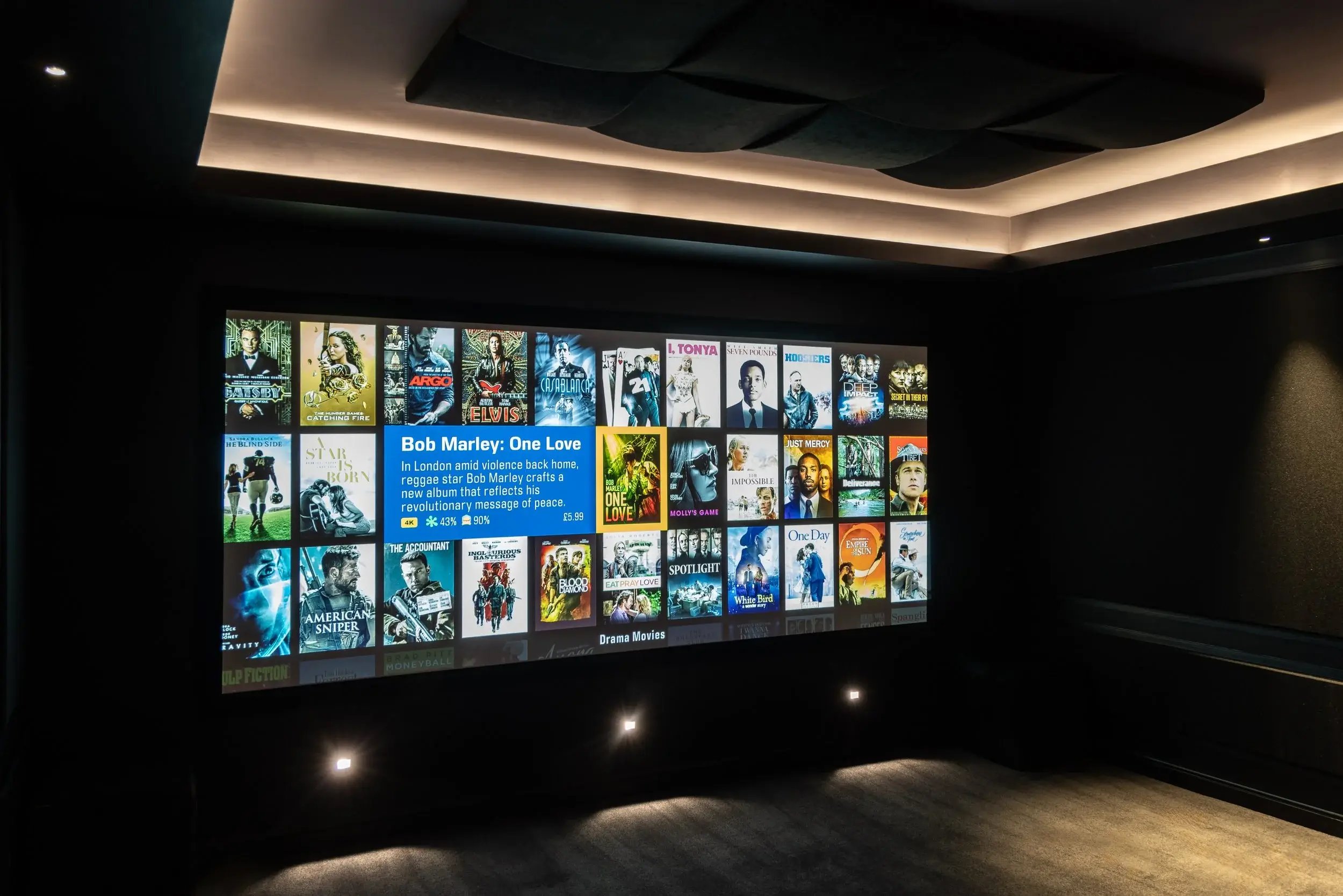Digital screen displaying a selection of movie posters in a dark room, with a highlighted feature about Bob Marley: One Love.