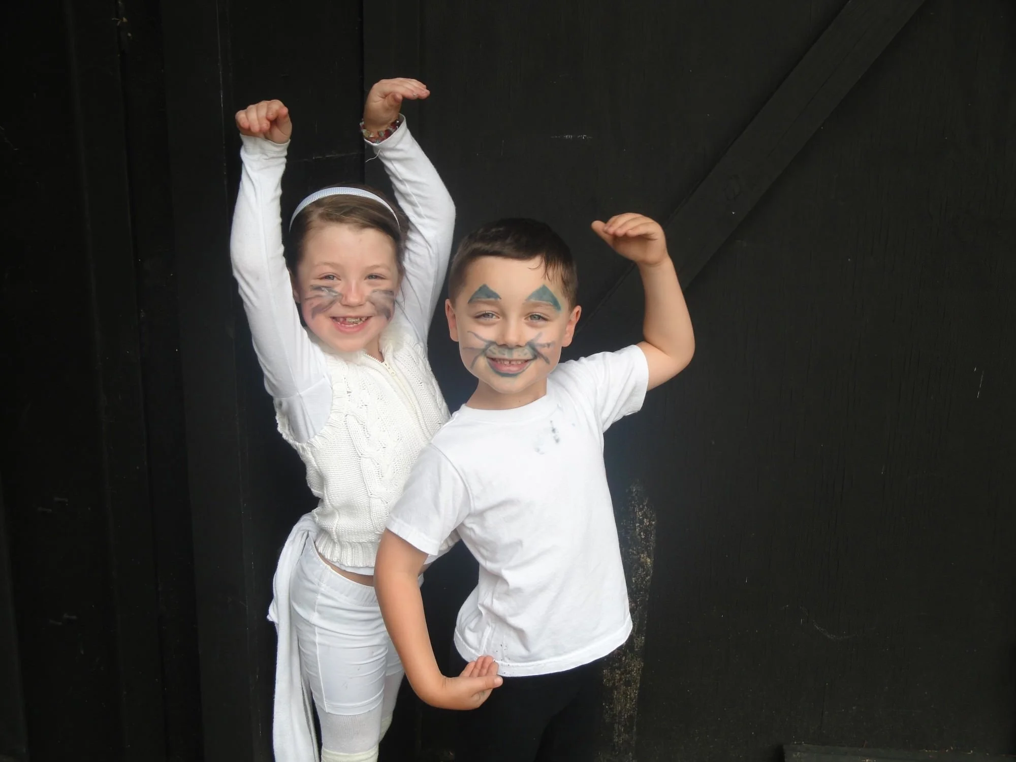 Two children standing with face paint, smiling and posing like the Cats from the musical Cats.