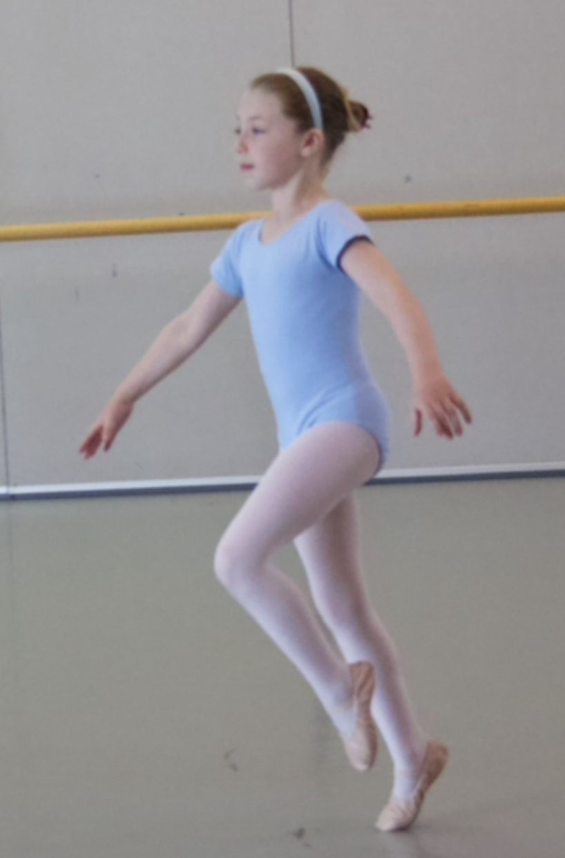 A young girl practicing ballet in a dance studio, wearing a light blue leotard and pink tights.