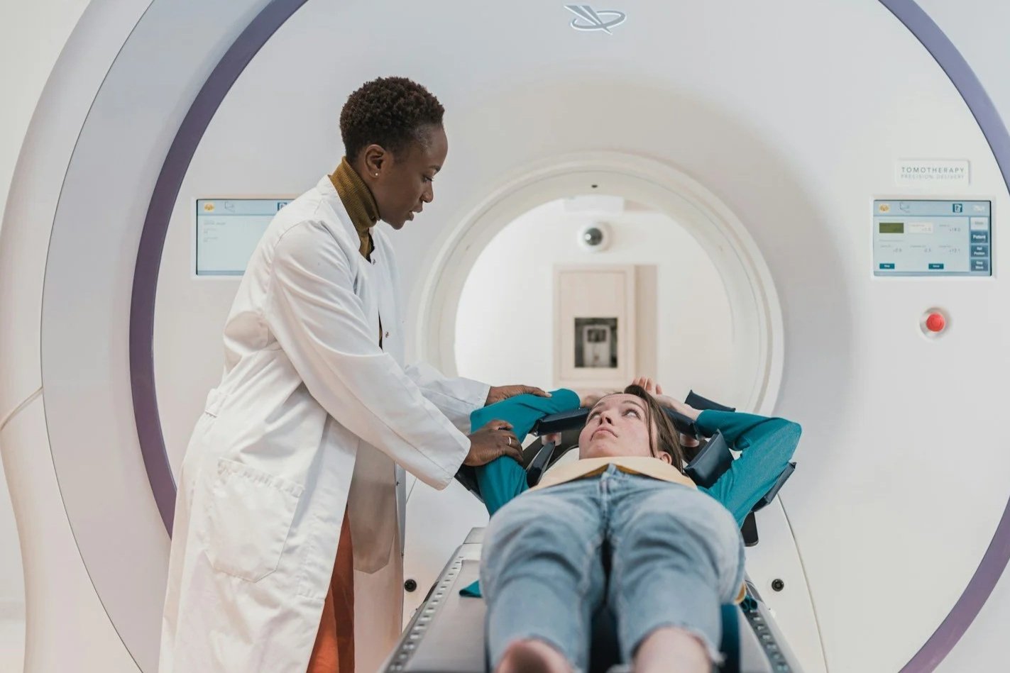 A healthcare professional assists a young woman during a medical scan in an MRI machine.