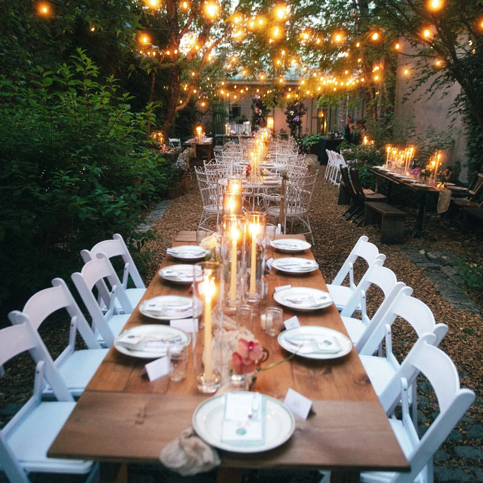 KRAUS folding farm table with end extension leaves set for an outdoor dinner under string lights