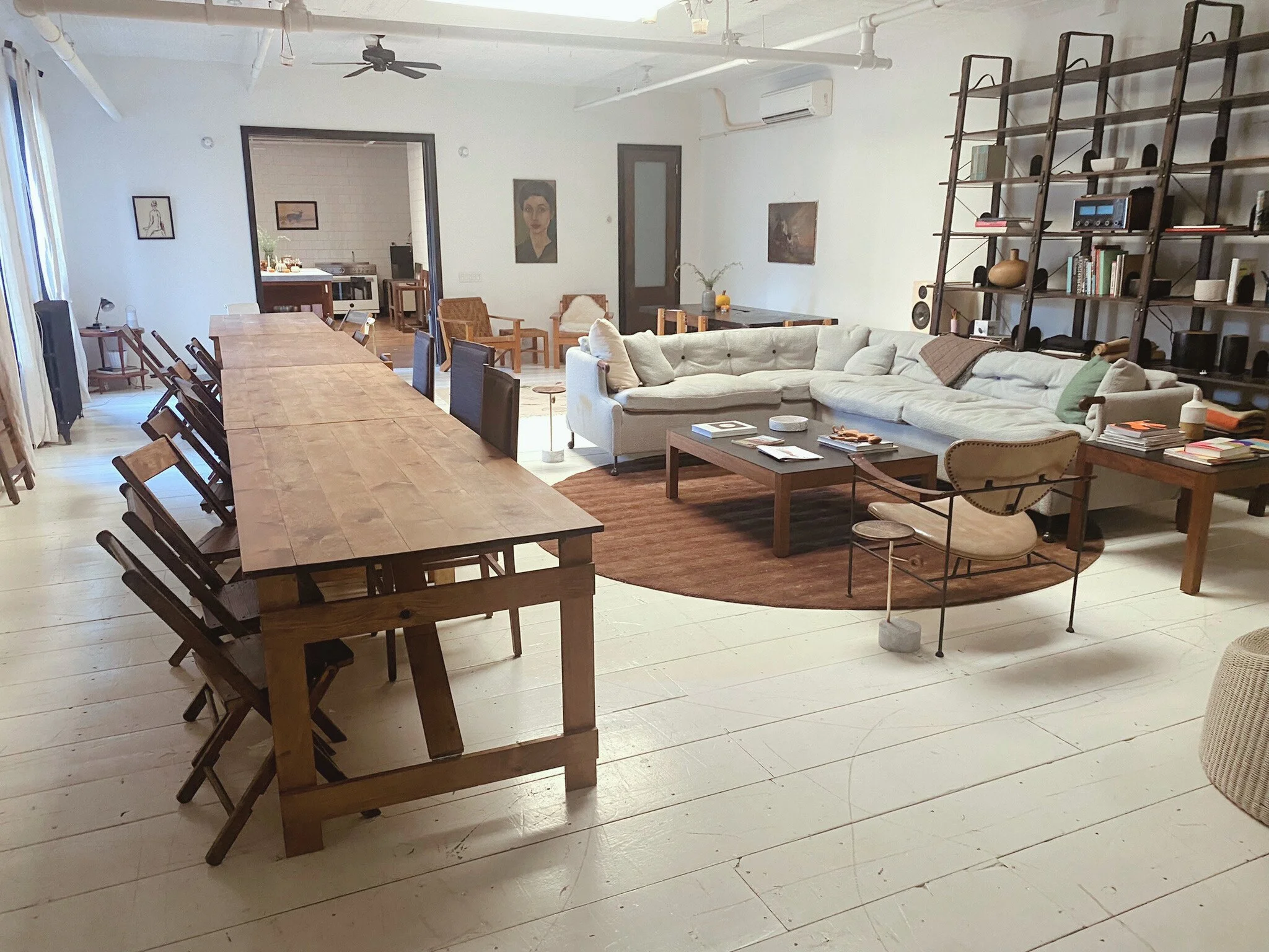 A long handmade folding farm table with vintage wooden folding chairs in a spacious lower Manhattan loft with a sofa and industrial bookshelves in the background.