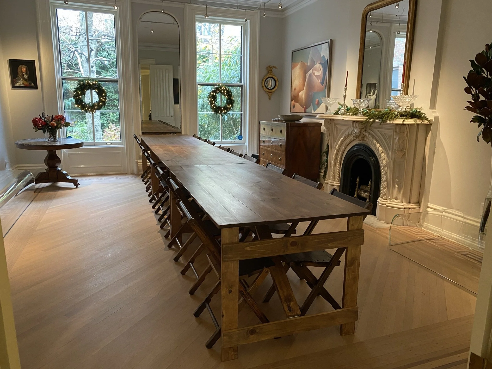 Long banquet of handmade folding farm tables and vintage wooden folding chairs in an elegant Brooklyn Heights townhouse decorated for Christmas with wreaths in the windows.