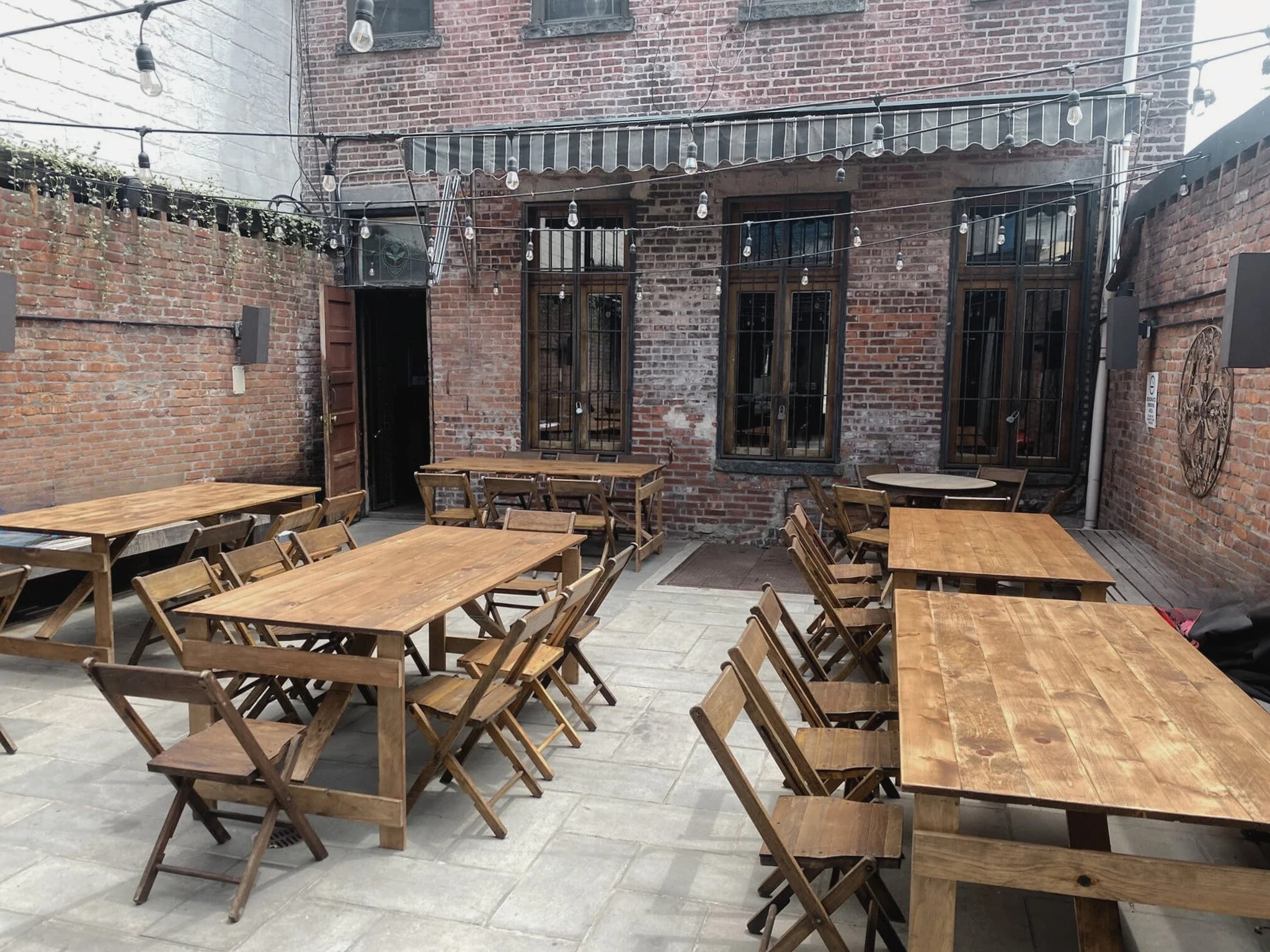 Several handmade folding farm tables with vintage wooden folding chairs in the backyard patio of LIC Bar in Long Island City Queens.