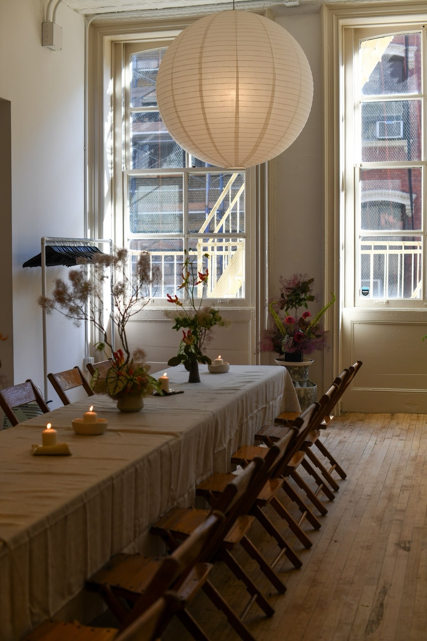 A long dining table with vintage wooden folding chairs set in a room with dramatic natural light coming from two big windows.