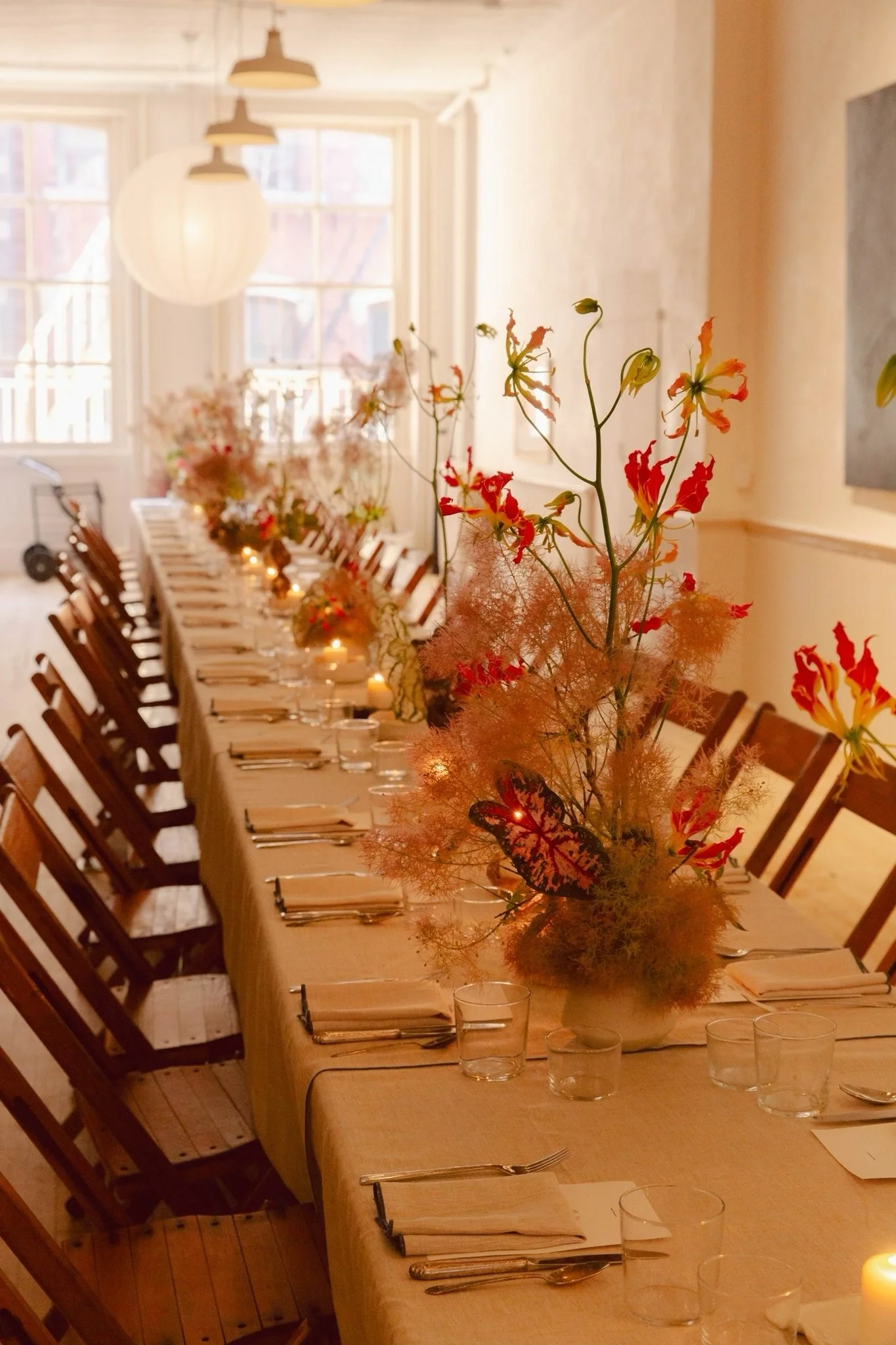 A long dining table with vintage wooden folding chairs set in a bright room with windows and pendant lights.