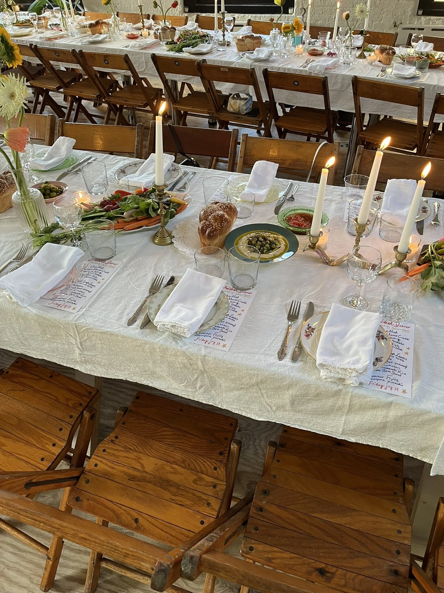 Set dining table decorated for a meal with view of vintage wooden folding chair seats, menus, place settings and candles.