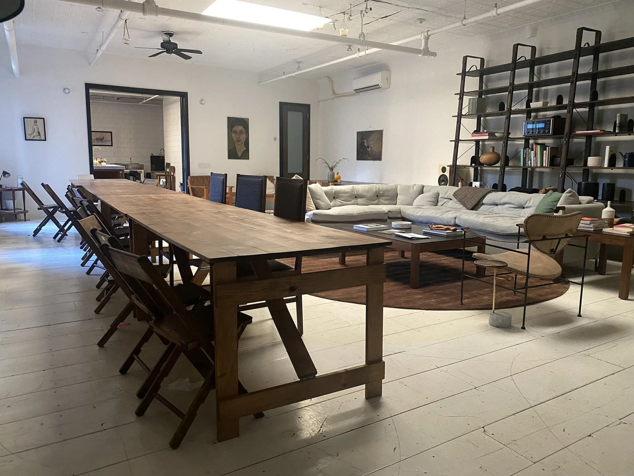 A long handmade folding farm table with vintage wooden folding chairs in a spacious lower Manhattan loft with a sofa and industrial bookshelves in the background.