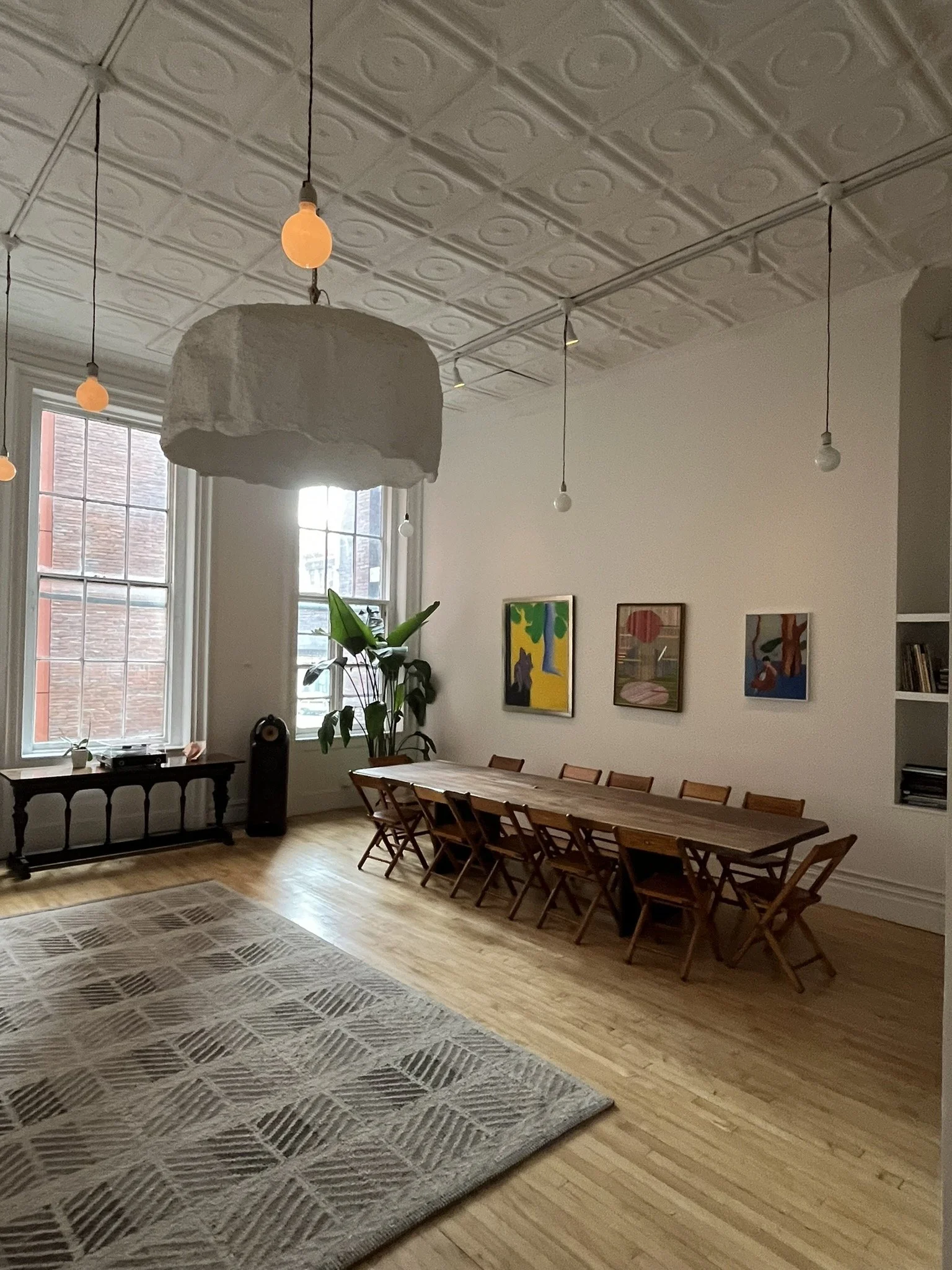 Vintage wooden folding chairs surrounding a long wooden table in a Tribeca artist's loft dining room with high ceilings, two large windows, and an abstract painting.