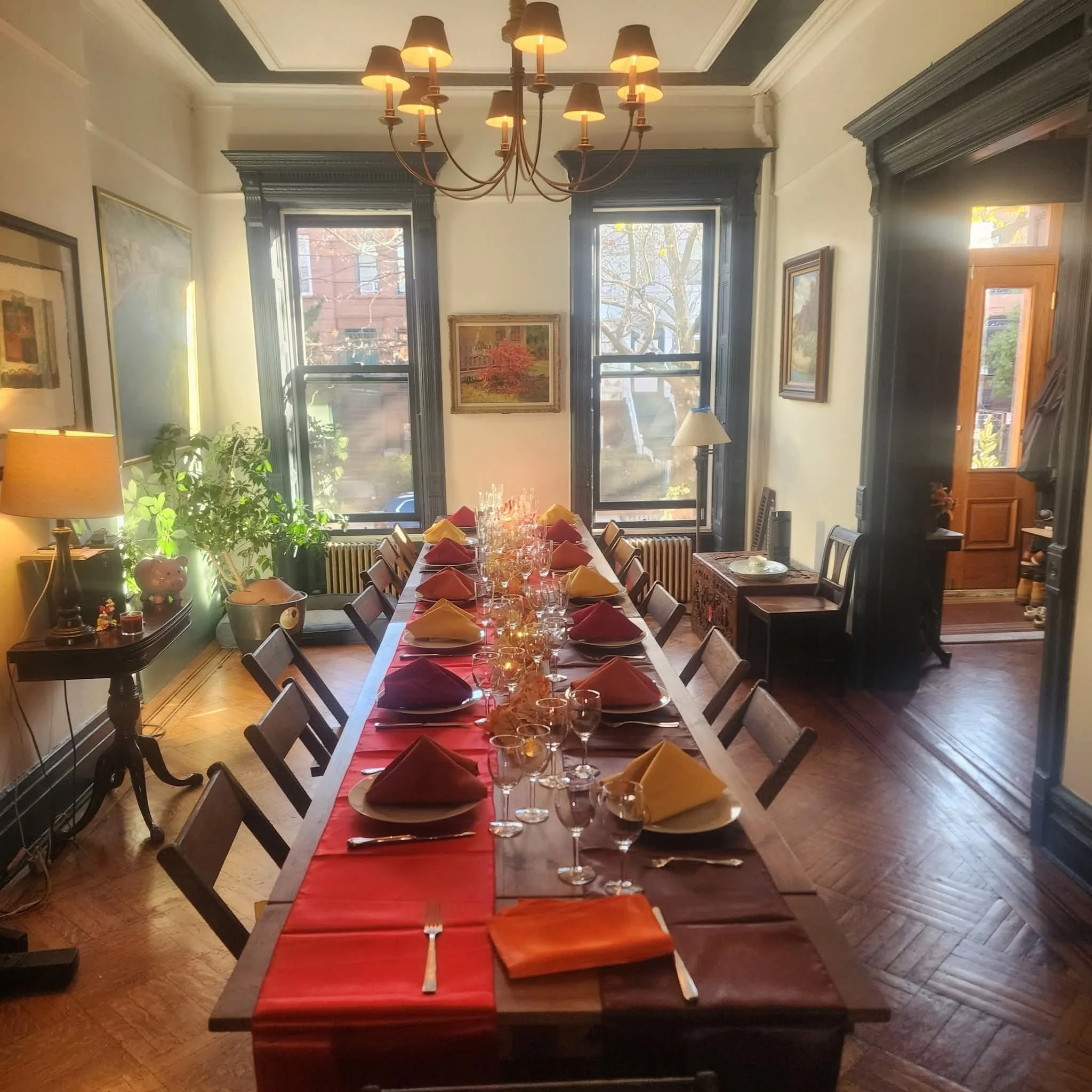 A handmade folding farm table and vintage wooden folding chairs set for an intimate Thanksgiving dinner in a dining room in a Brooklyn brownstone with large windows and a chandelier.