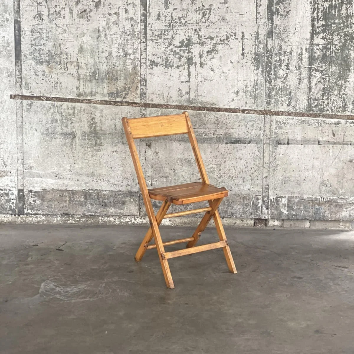 KRAUS light-finish vintage wooden folding chair against a concrete wall
