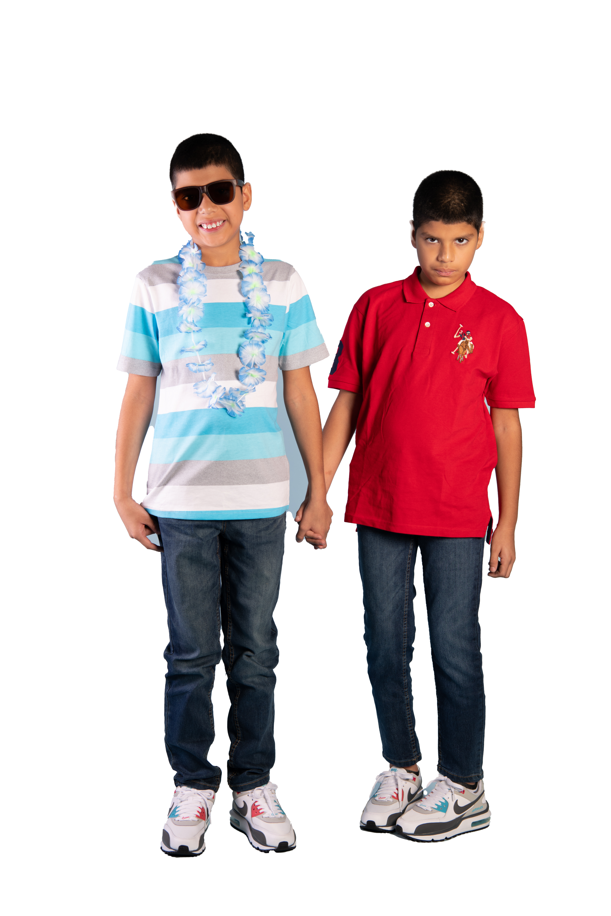 Two young boys holding hands, one smiling wearing sunglasses and a blue Hawaiian lei, the other with a serious expression wearing a red Polo shirt.