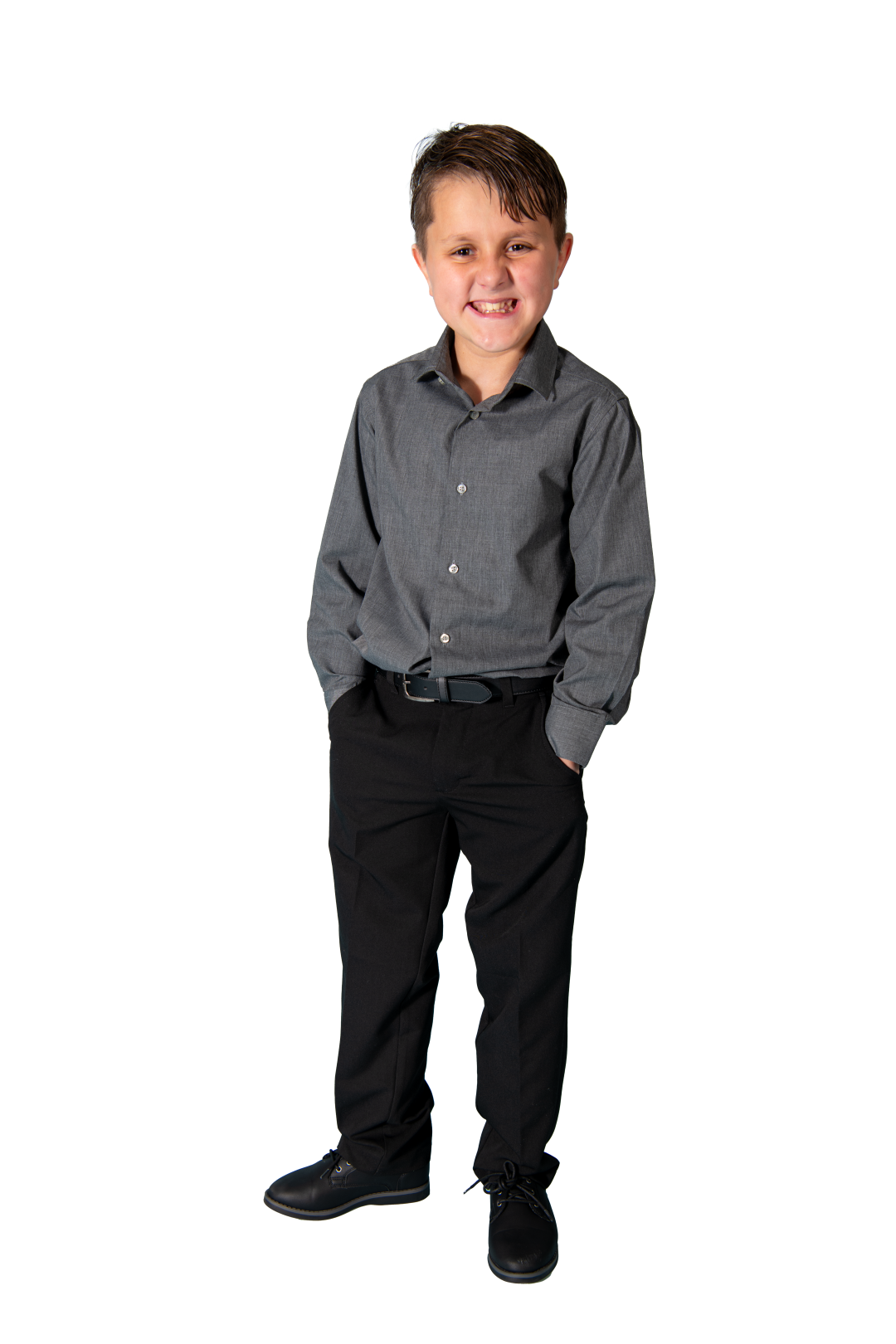 A young boy standing with his hands in his pockets, smiling, dressed in a grey button-up shirt and black pants, on a white background.