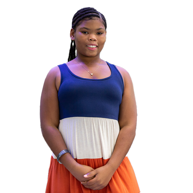 A young woman with braided hair wearing a sleeveless dress with a navy top, a beige middle section, and an orange skirt, standing against a black background.