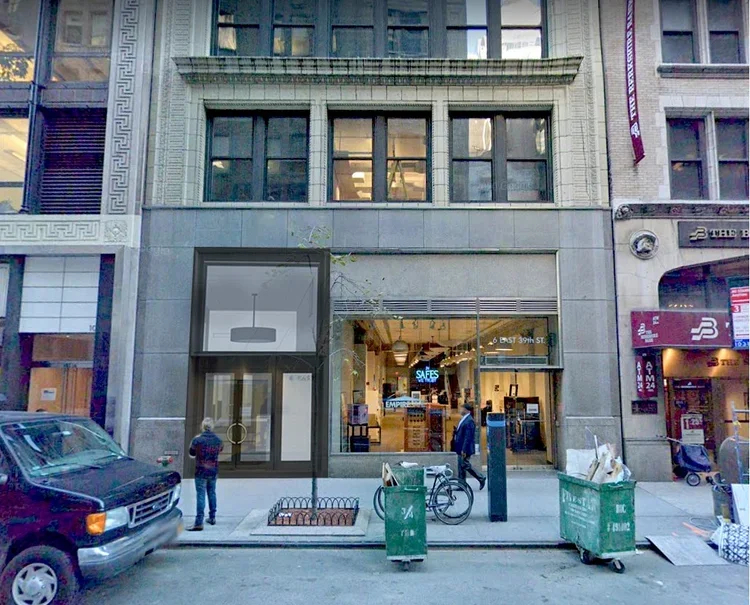 Street view of the TNY Therapists of New York building in midtown Manhattan with a retail store entrance, two people walking by, parked car, bicycle, and trash bins.