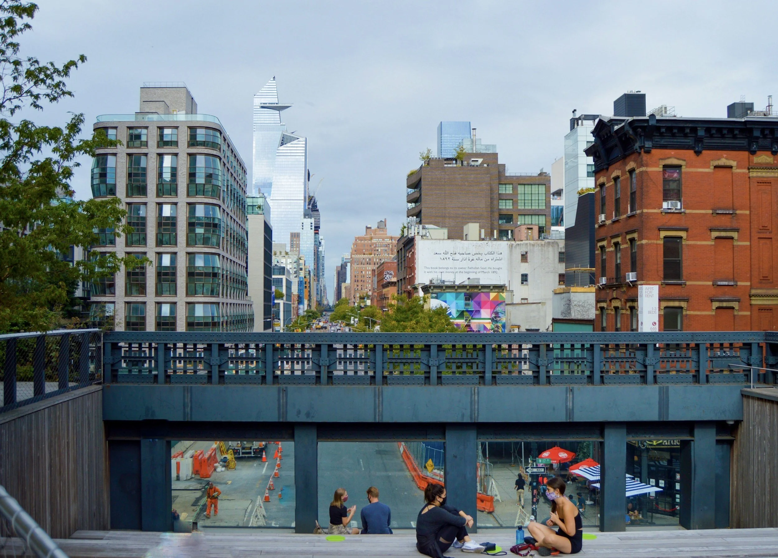 People sitting on a rooftop deck in an urban cityscape, with high-rise buildings and construction along the street below.