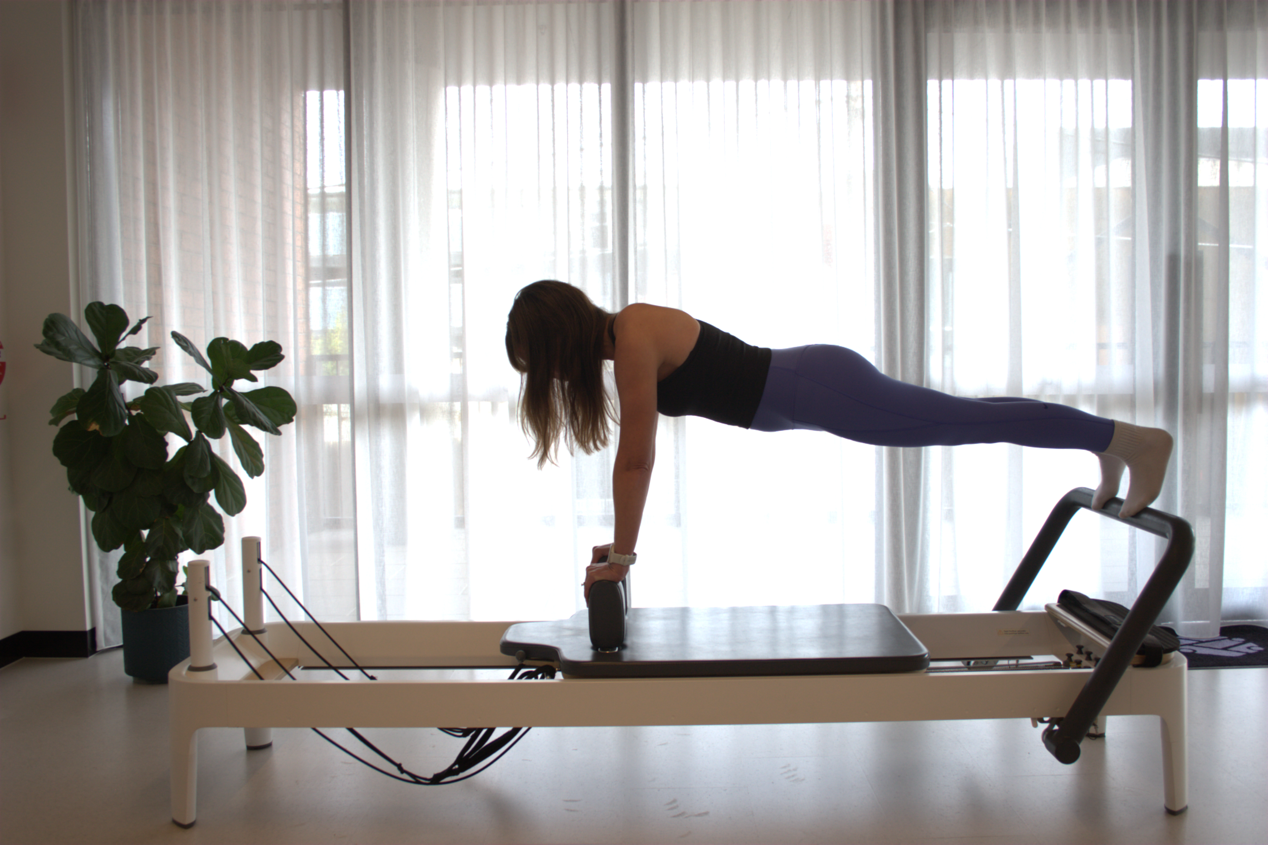 A woman in workout clothes using a Pilates reformer machine in a fitness studio.