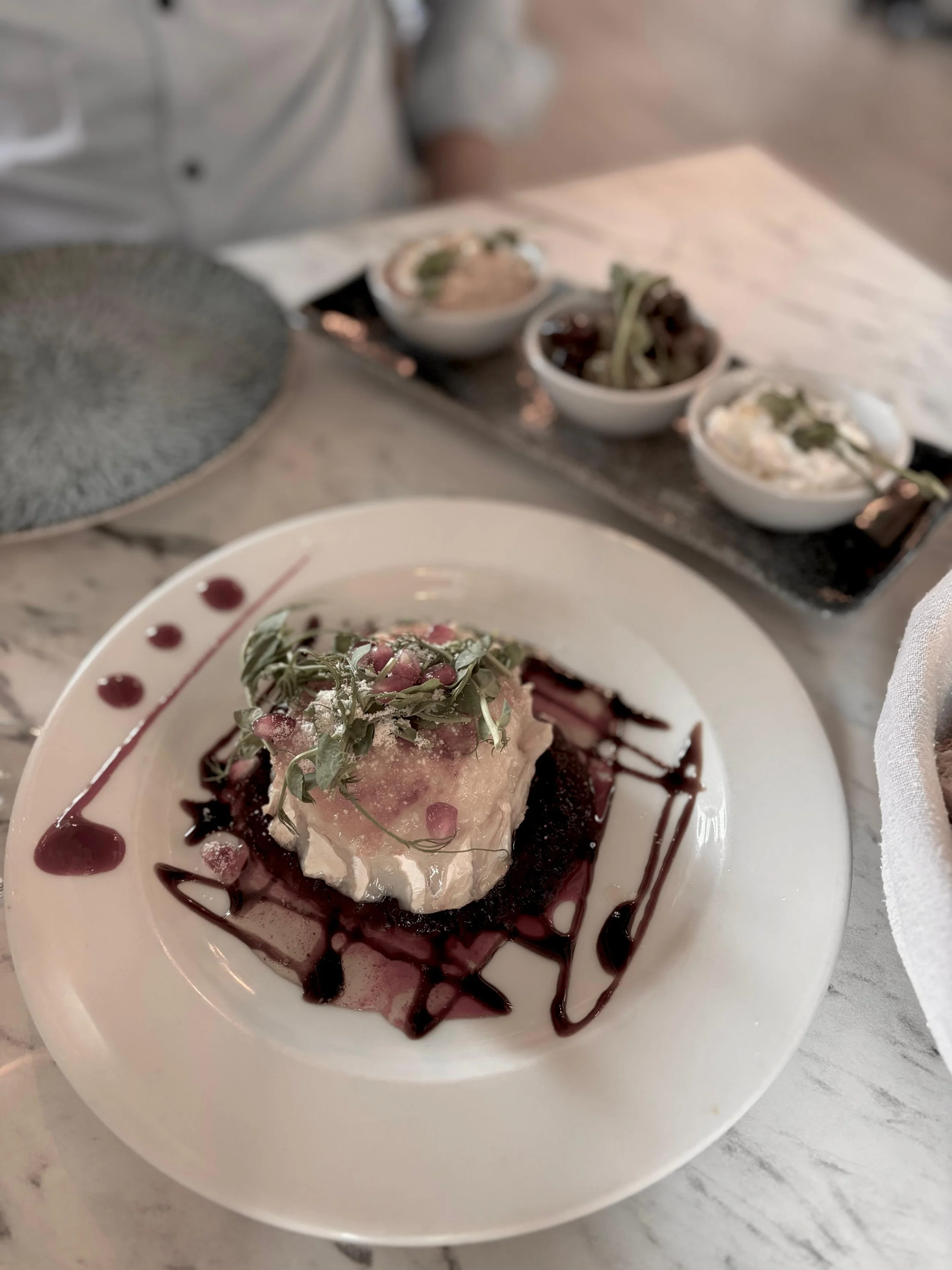 A beige ceramic vase with a simple design, holding a dried branch, sits on a wooden surface with sunlight casting shadows on a neutral wall.