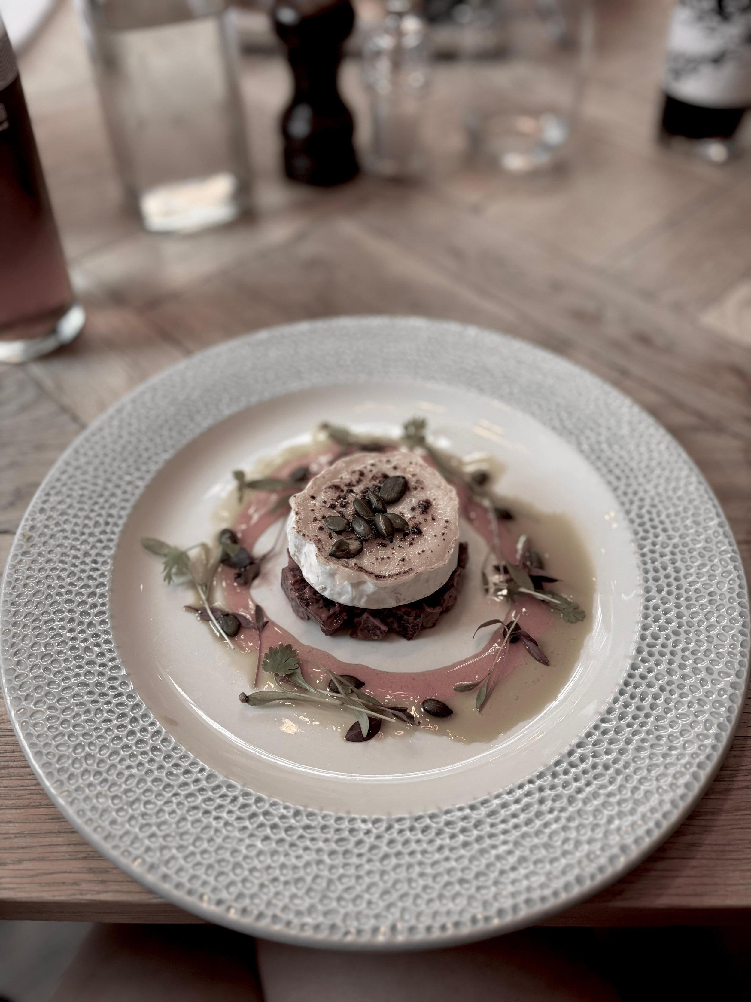 A beige ceramic vase with dried branches on a wooden surface, shadow cast on background wall.