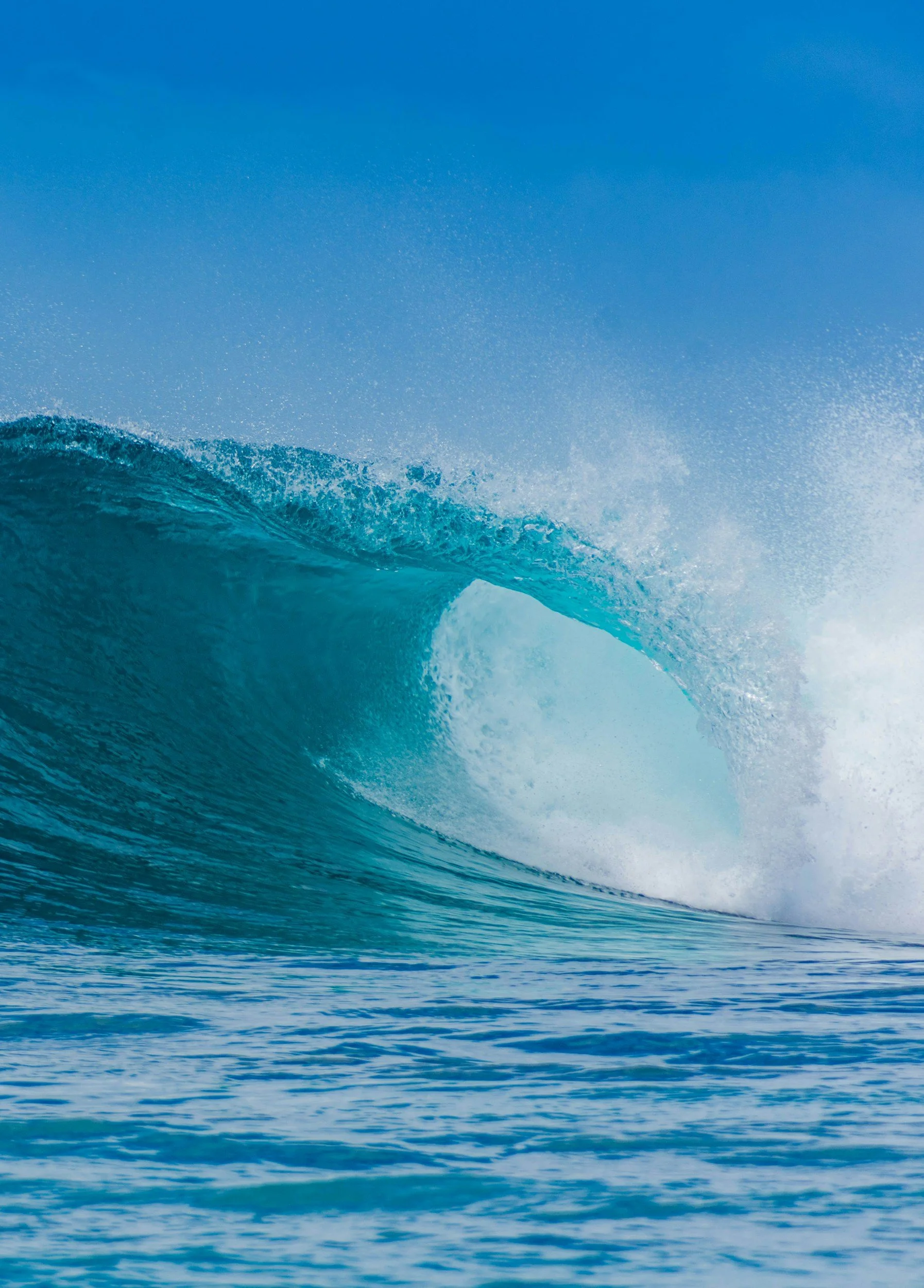 An ocean wave with water spray and a clear blue sky.