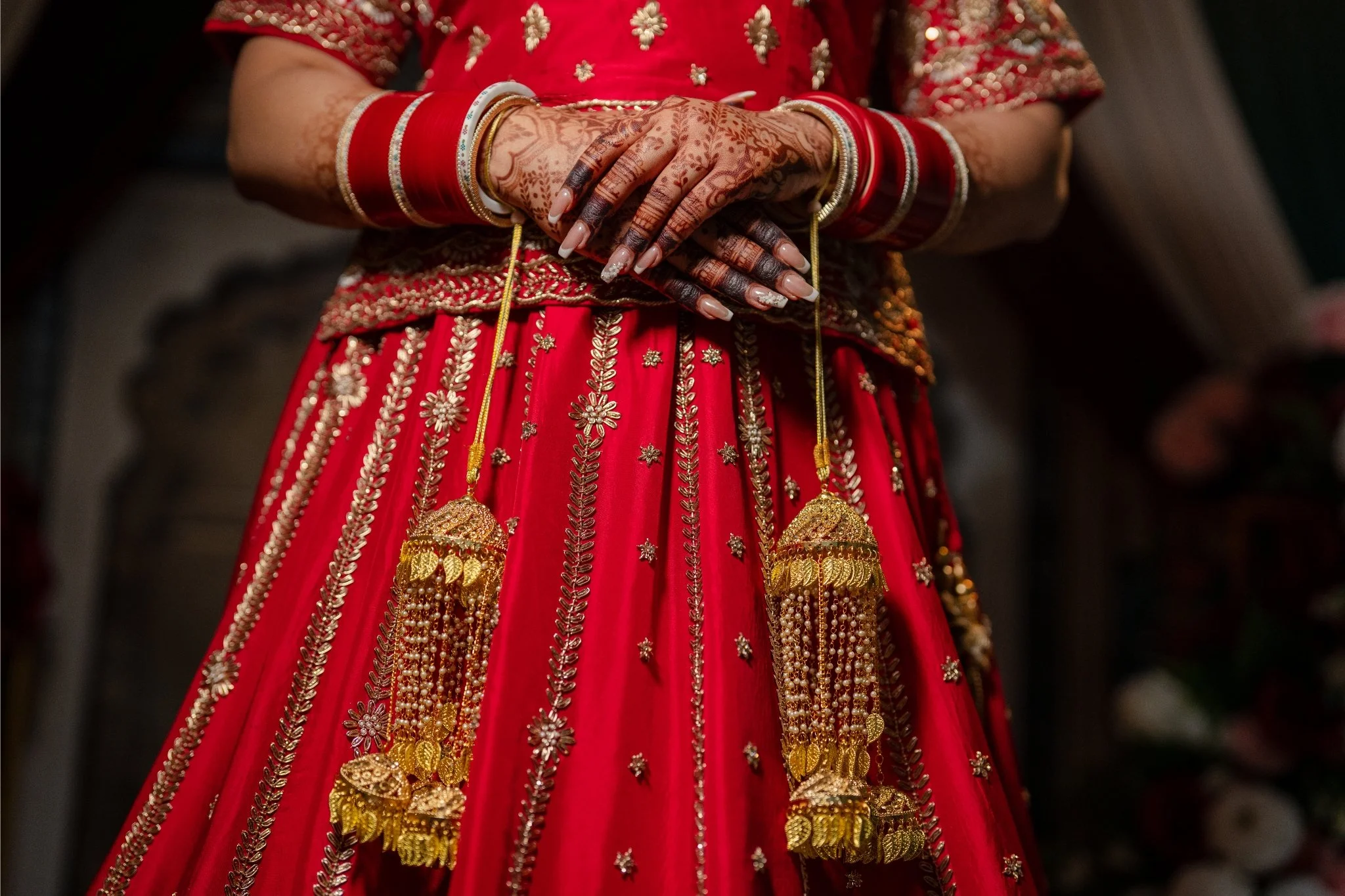 Close-up of a woman wearing traditional Indian bridal attire, a red dress with gold embroidery, and intricate henna designs on her hands with red and gold bangles.
