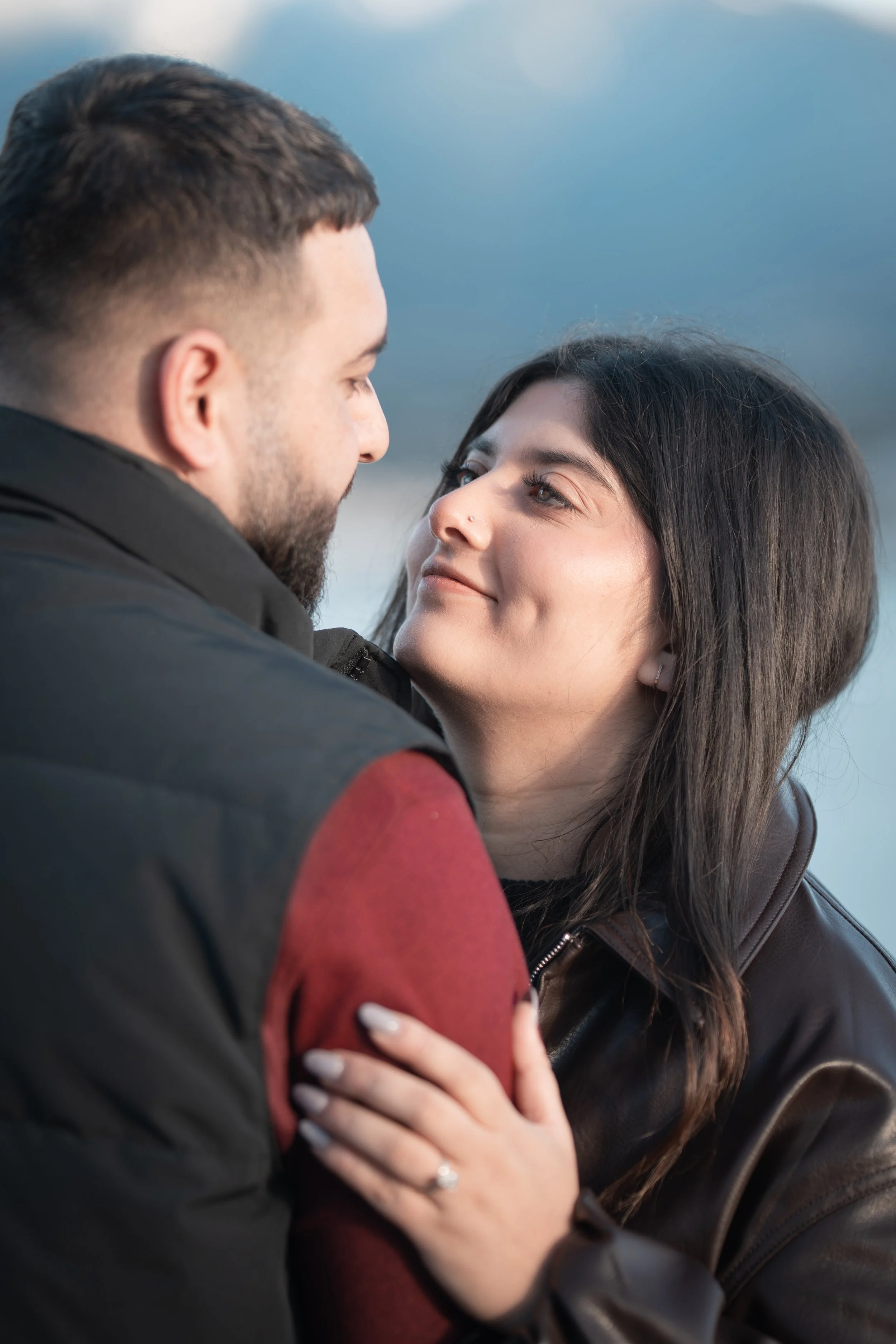 A man and woman looking into each other's eyes lovingly outdoors with a cloudy sky background.