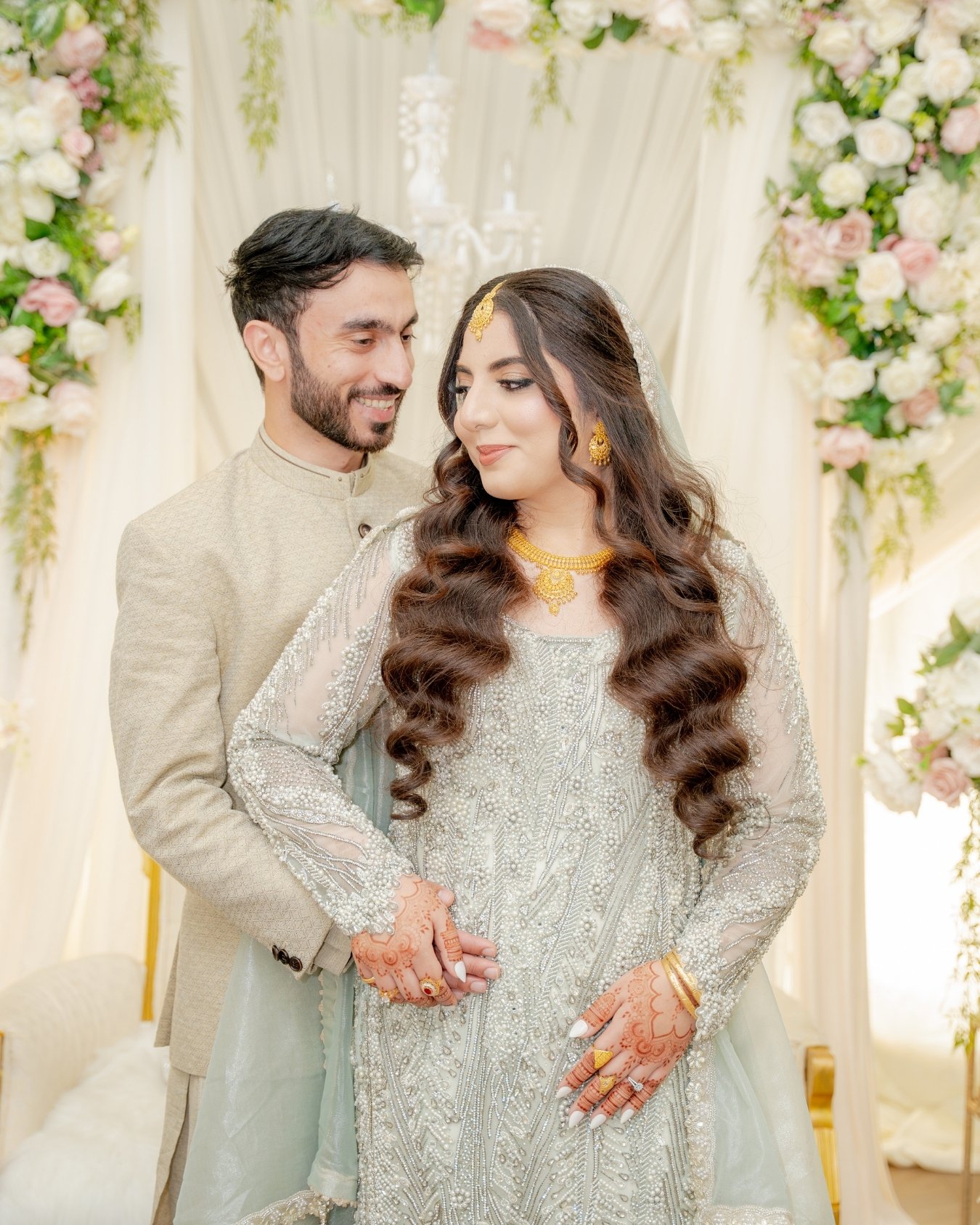 A bride and groom standing close together during their wedding, surrounded by floral decorations. Nikkah couple shoot, nikkah couple photos, nikka photoshoot