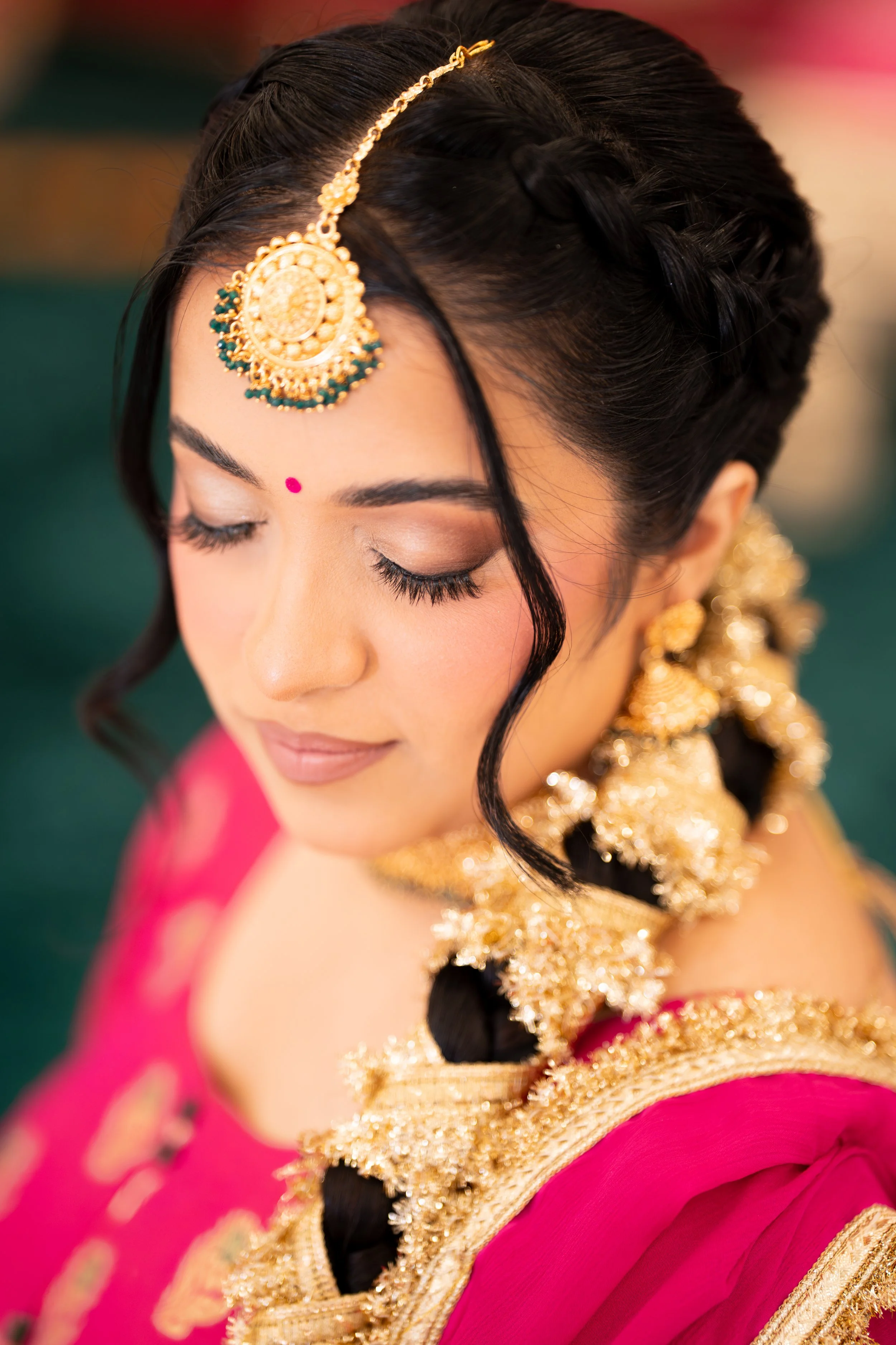 Close-up of a woman in traditional Indian attire with ornate gold jewelry, red bindi, and pink saree with gold accents, with her eyes closed and a gentle expression. Jaggo outfits
