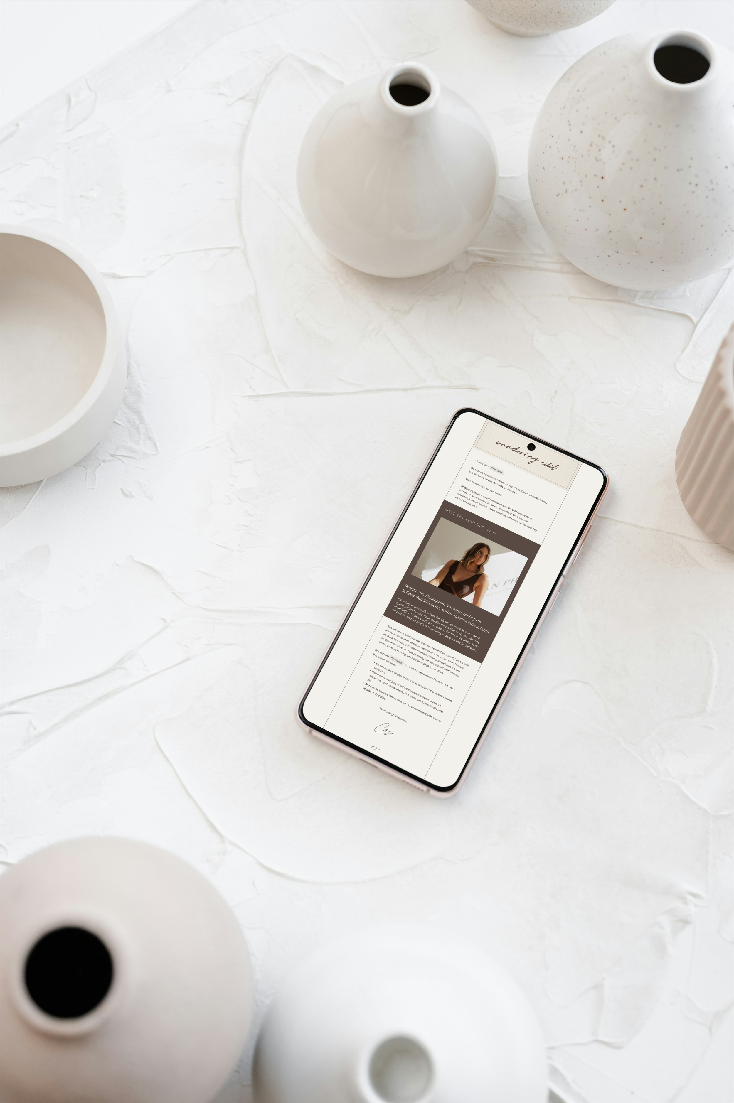 A phone among ceramic vases displays The Wandering Edit, Wanders Studio's email newsletter designed for entrepreneurs.