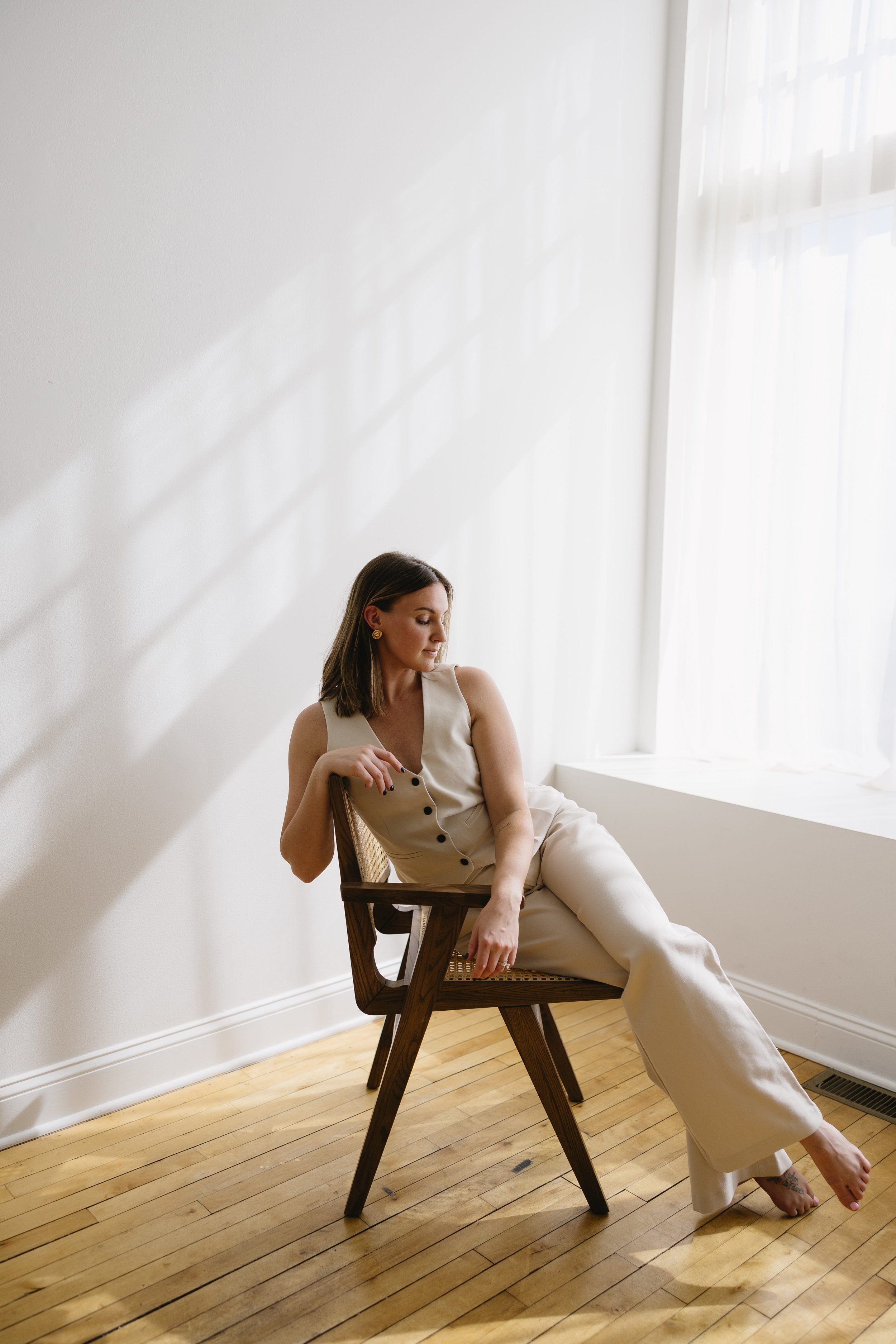 Cassie West, founder of Wanders Studio, seated in a cane chair in a sunlit white studio in neutral tones.