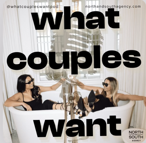 Two women wearing black outfits and sunglasses relaxing in a white bathtub with their arms stretched out, holding each other's hands, inside a bright room with large windows and decorated walls.