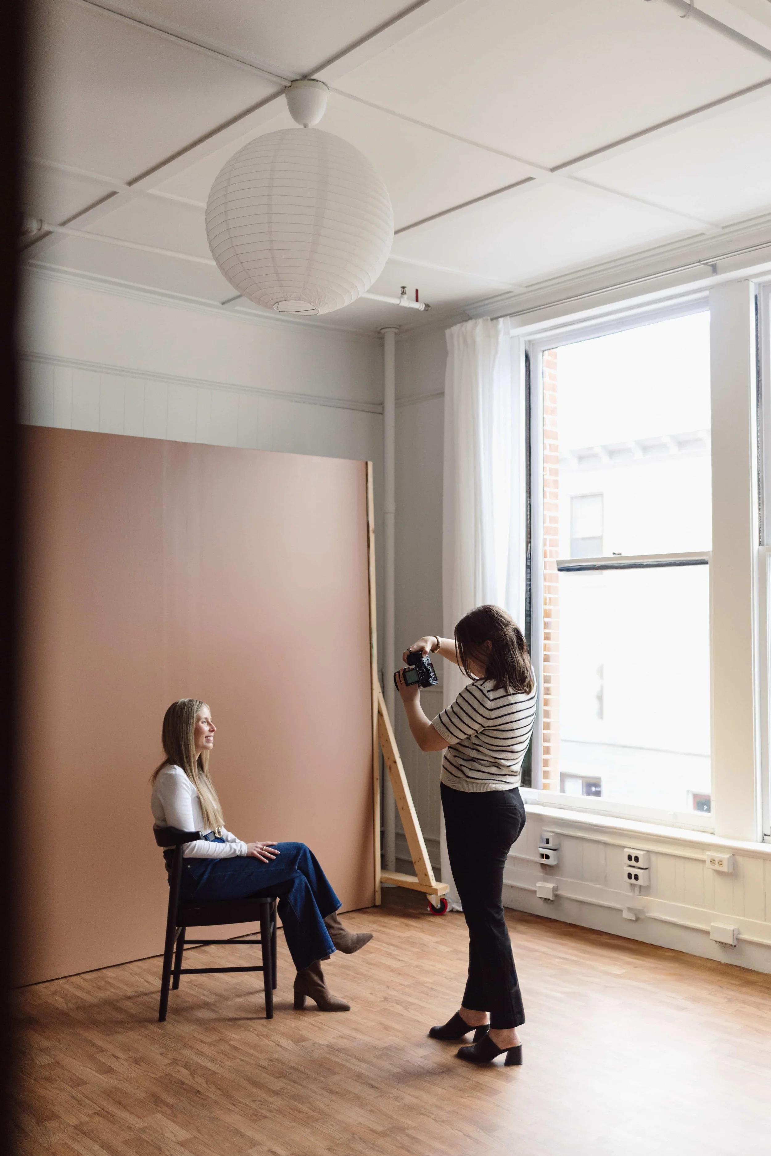 Rebecca Loomis, NY Capital Region brand photographer in studio taking photos of a client sitting down near a large window