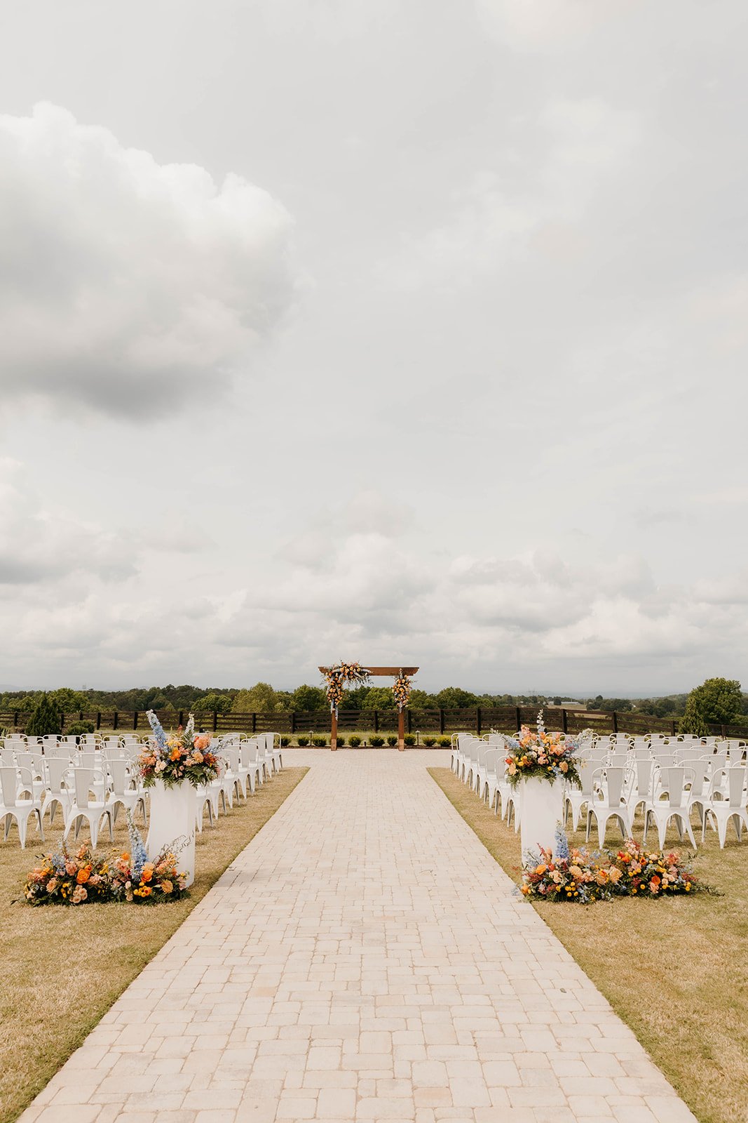 Outdoor wedding ceremony setup with chairs, floral arrangements, and an arch on a cloudy day.