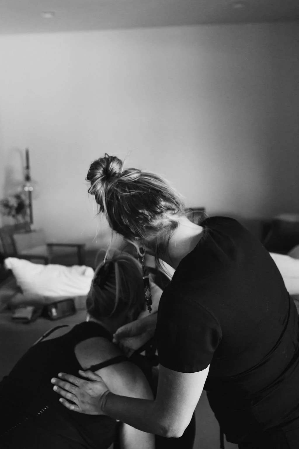 A woman receiving a massage in a room with a bed and nightstand, in black and white.