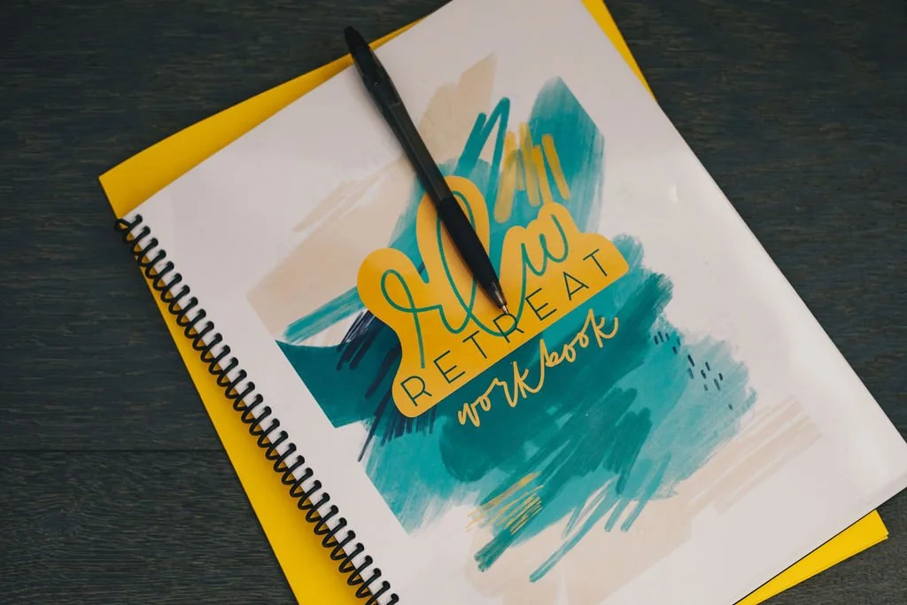 A spiral-bound notebook titled "Hello Retirement" with a pen resting on it, placed on a dark wooden surface.