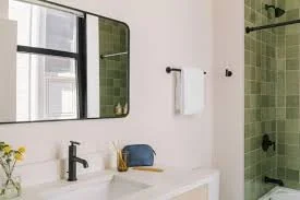 Bathroom with a white vanity, a black faucet, a mirror, and a shower with green tiles.