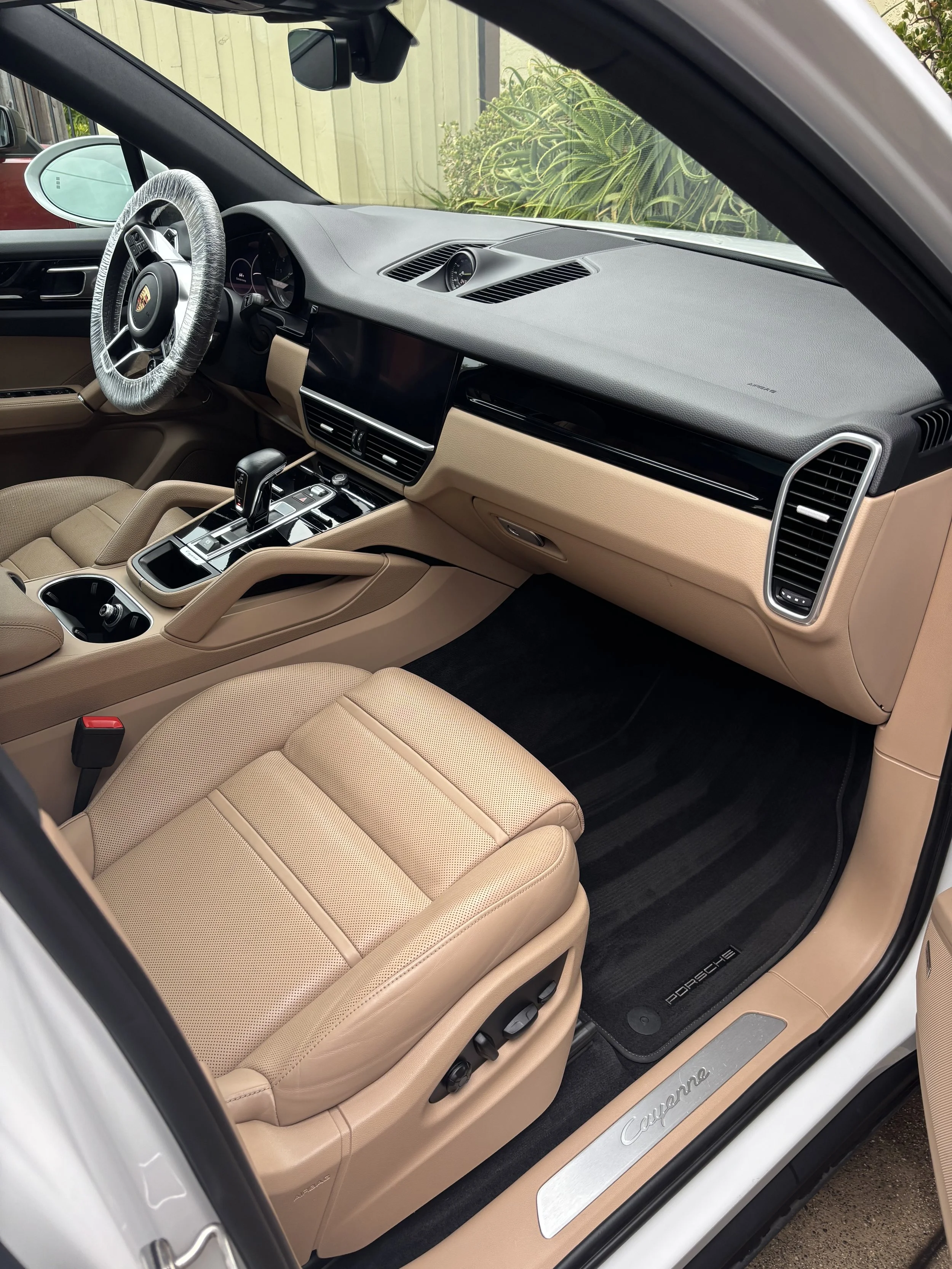 Interior view of a beige-colored Porsche Cayenne with a black dashboard, steering wheel, and center console, and beige leather seats.