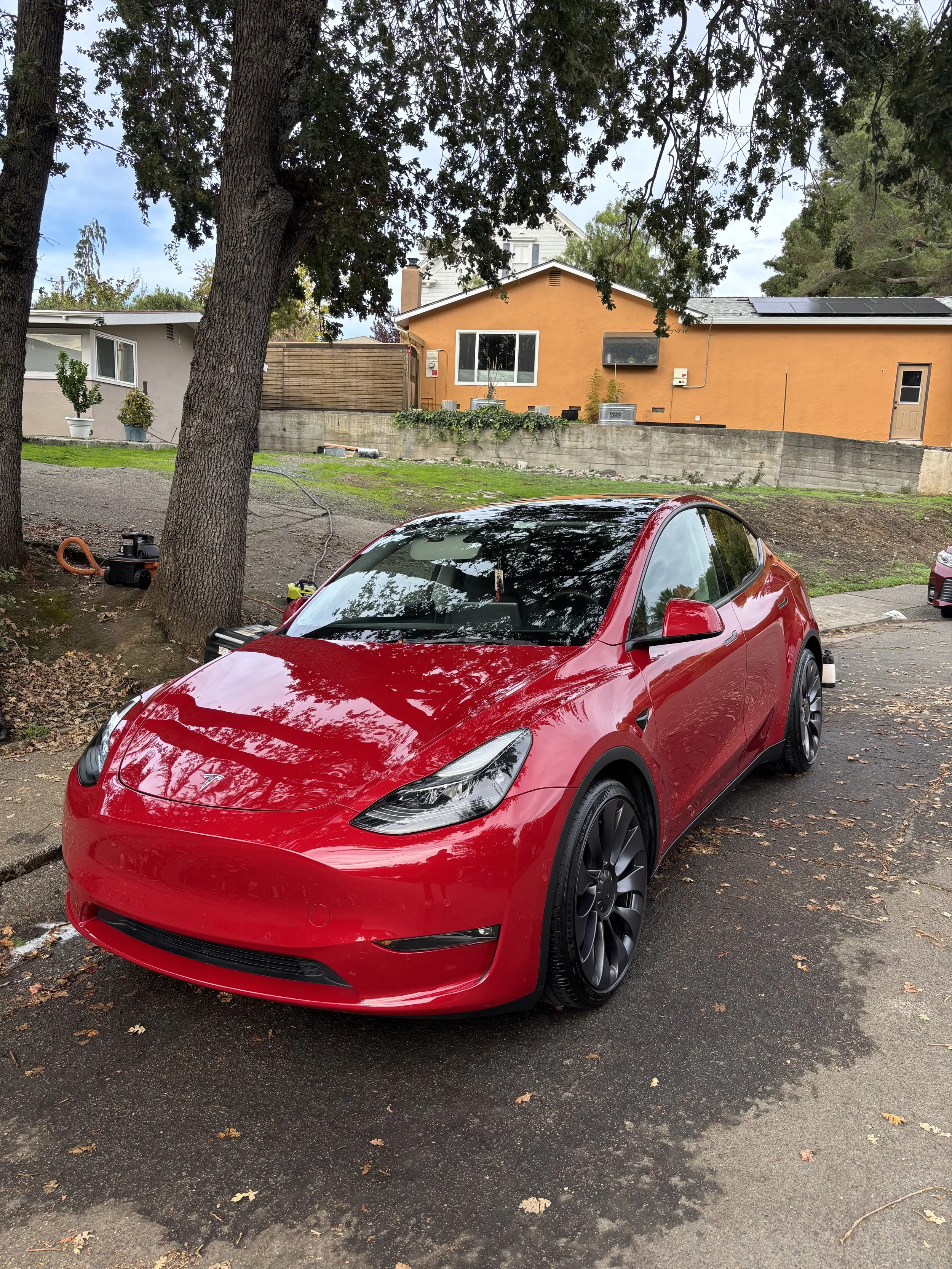 Red sporty compact car parked on a street with trees and residential houses in the background.